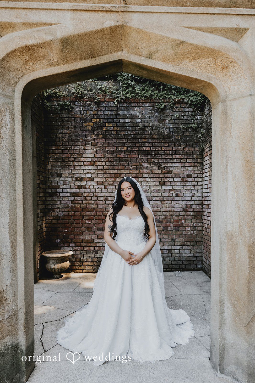 Sharmaine + Ronald A bride standing in a stone archway with her long train extended.