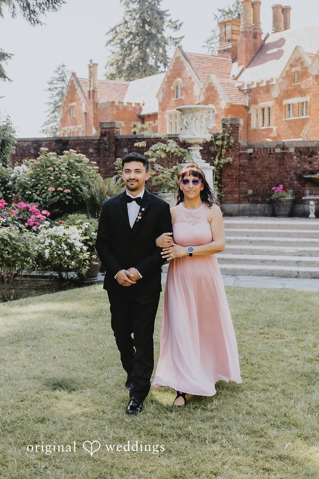 Sharmaine + Ronald A groom in a suit walking next to a woman in a pink dress on a paved path.
