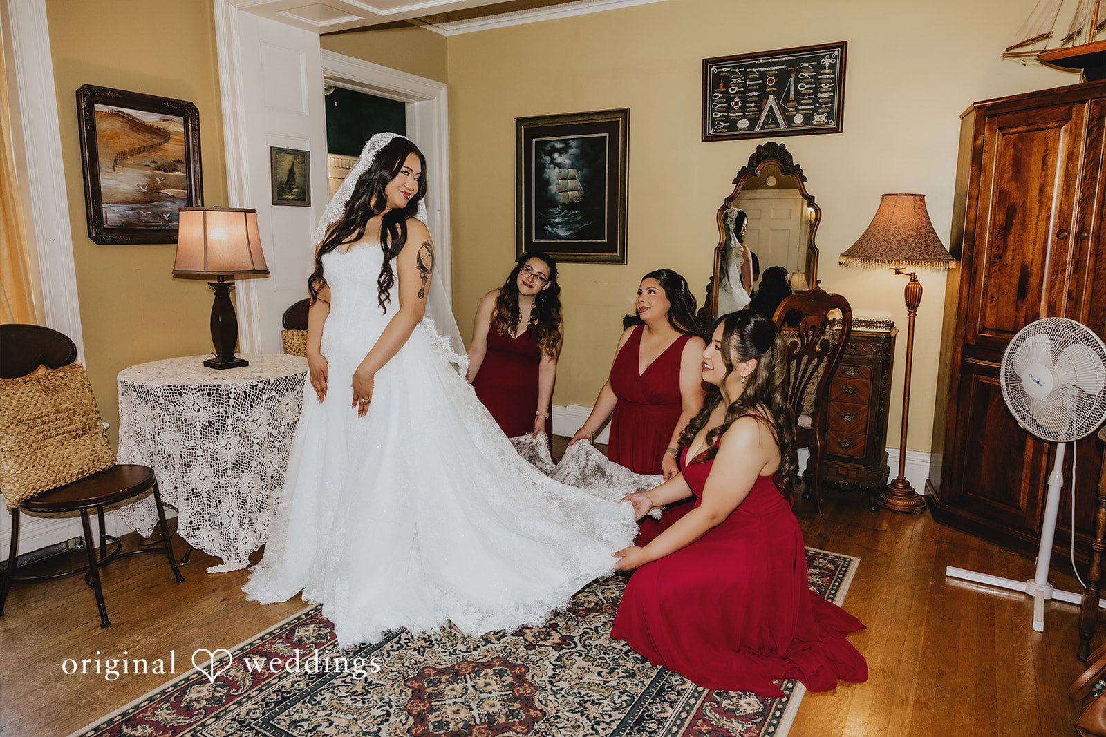 Sharmaine + Ronald A bride having her dress adjusted by a bridesmaid in a red gown.