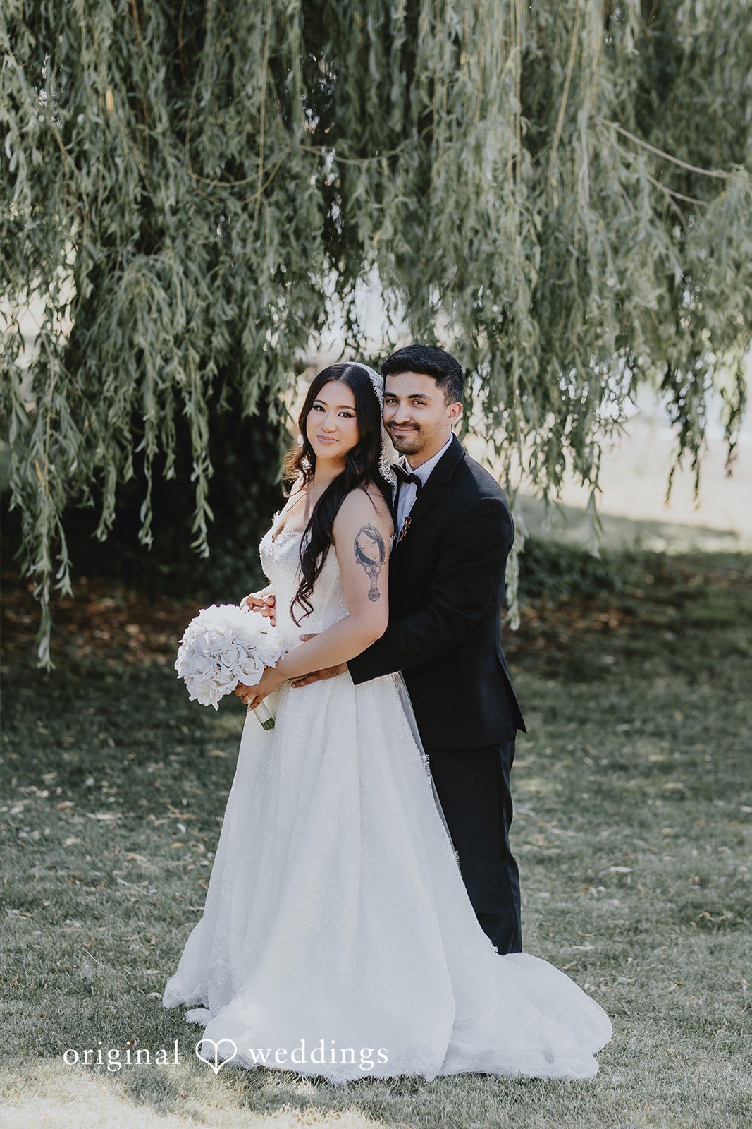 Sharmaine + Ronald A bride and groom posing together while standing on a grassy field.