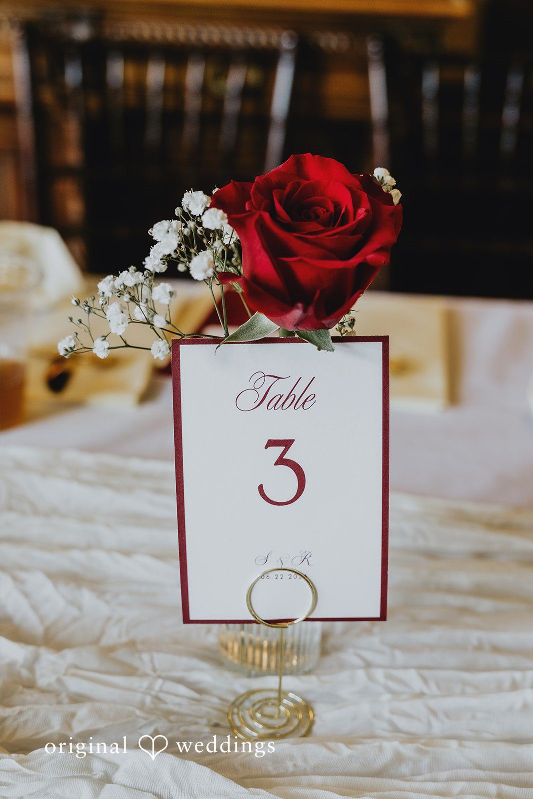 Sharmaine + Ronald A wedding reception table number card sitting next to a red flower.