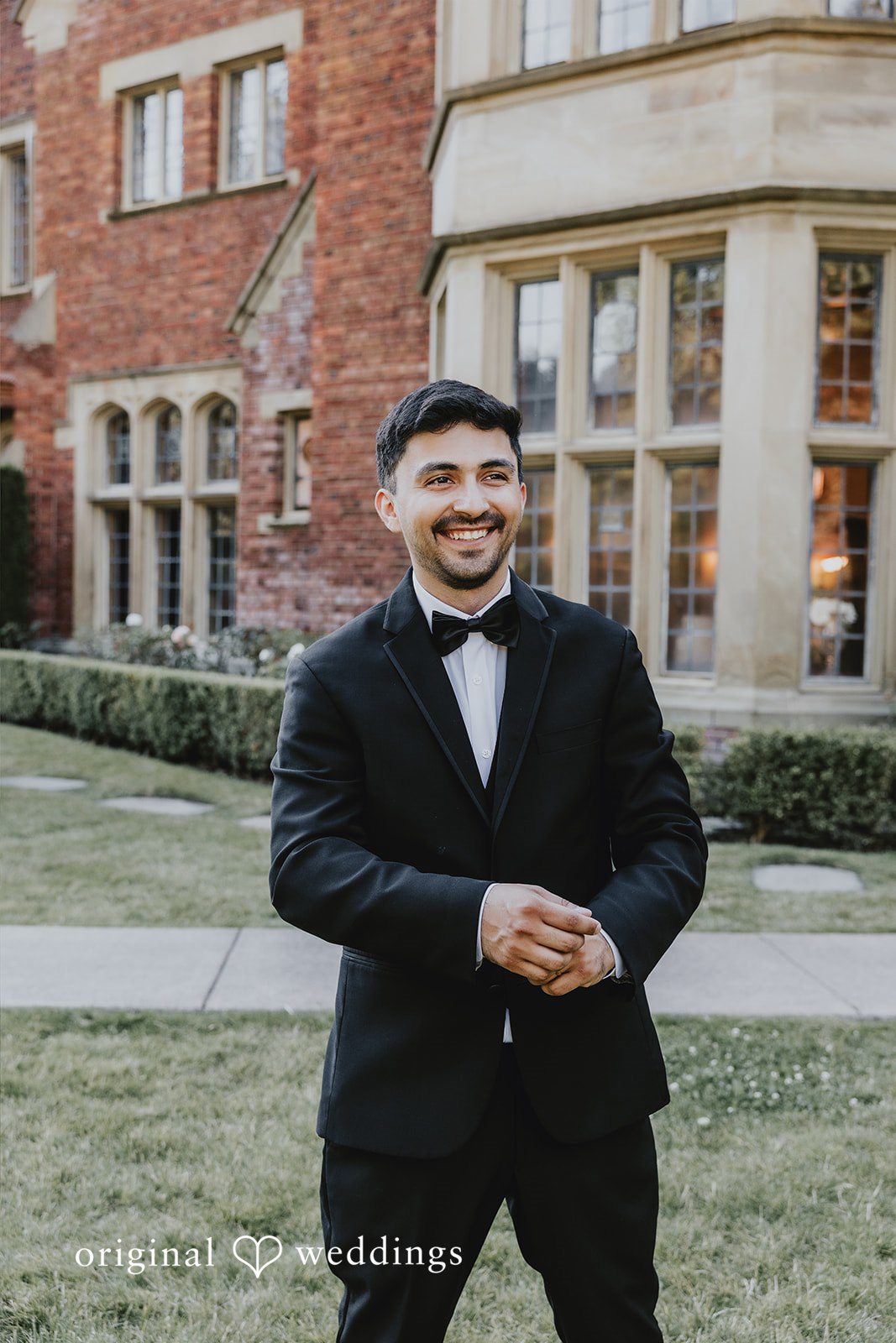 Sharmaine + Ronald A smiling groom wearing a black tuxedo in front of a stone building.