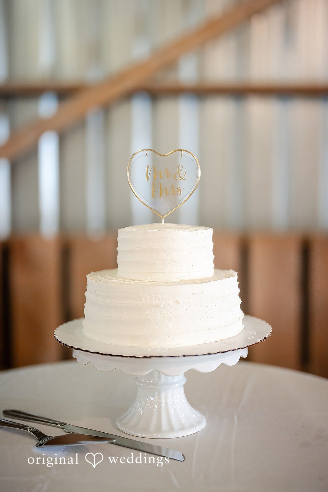 Kayla + Dillon A simple, elegant multi-tiered white wedding cake resting on a serving stand.