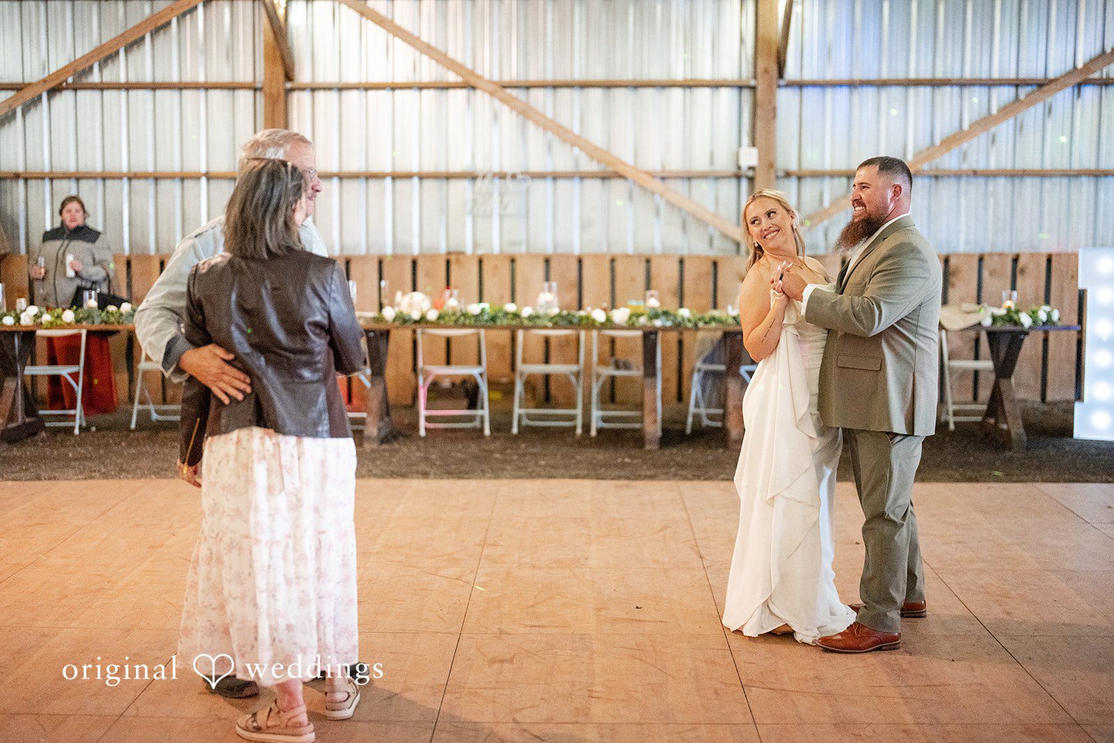Kayla + Dillon A bride and groom standing on the reception dance floor while looking toward a guest speaking.