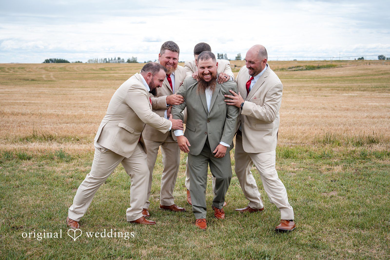 Kayla + Dillon A groom and his groomsmen sharing a laugh and posing playfully in an open field.