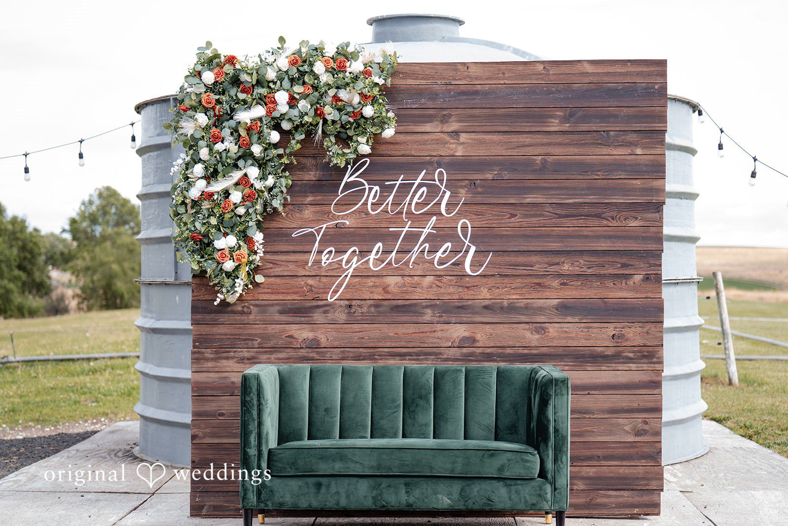 Kayla + Dillon A green velvet couch placed in front of a rustic wooden backdrop decorated with greenery.