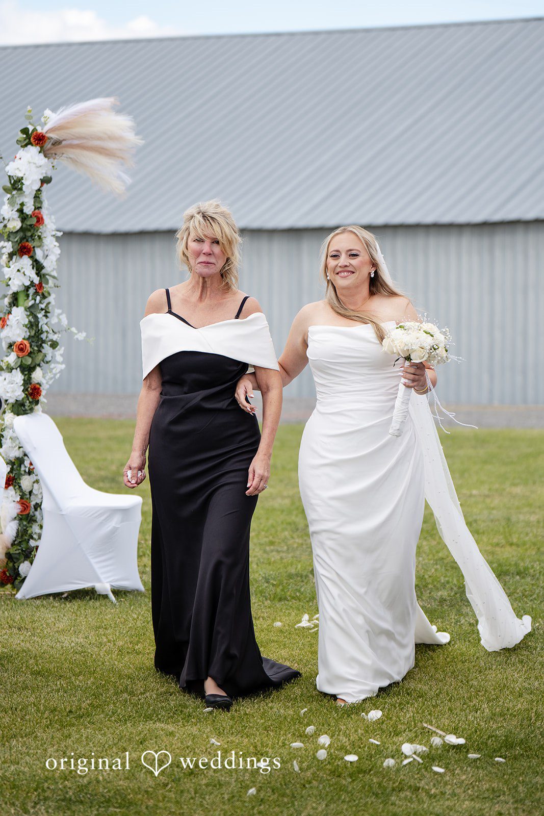 Kayla + Dillon Two women walking down the grassy aisle together towards the wedding setup.