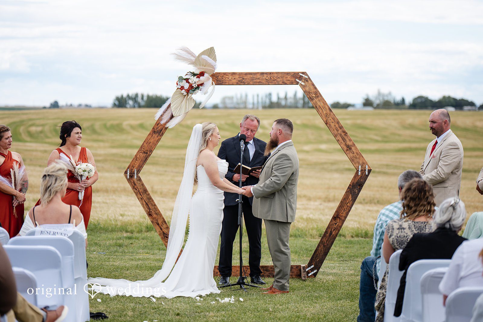 Kayla + Dillon A bride and groom holding hands during their ceremony in front of a hexagonal arch.
