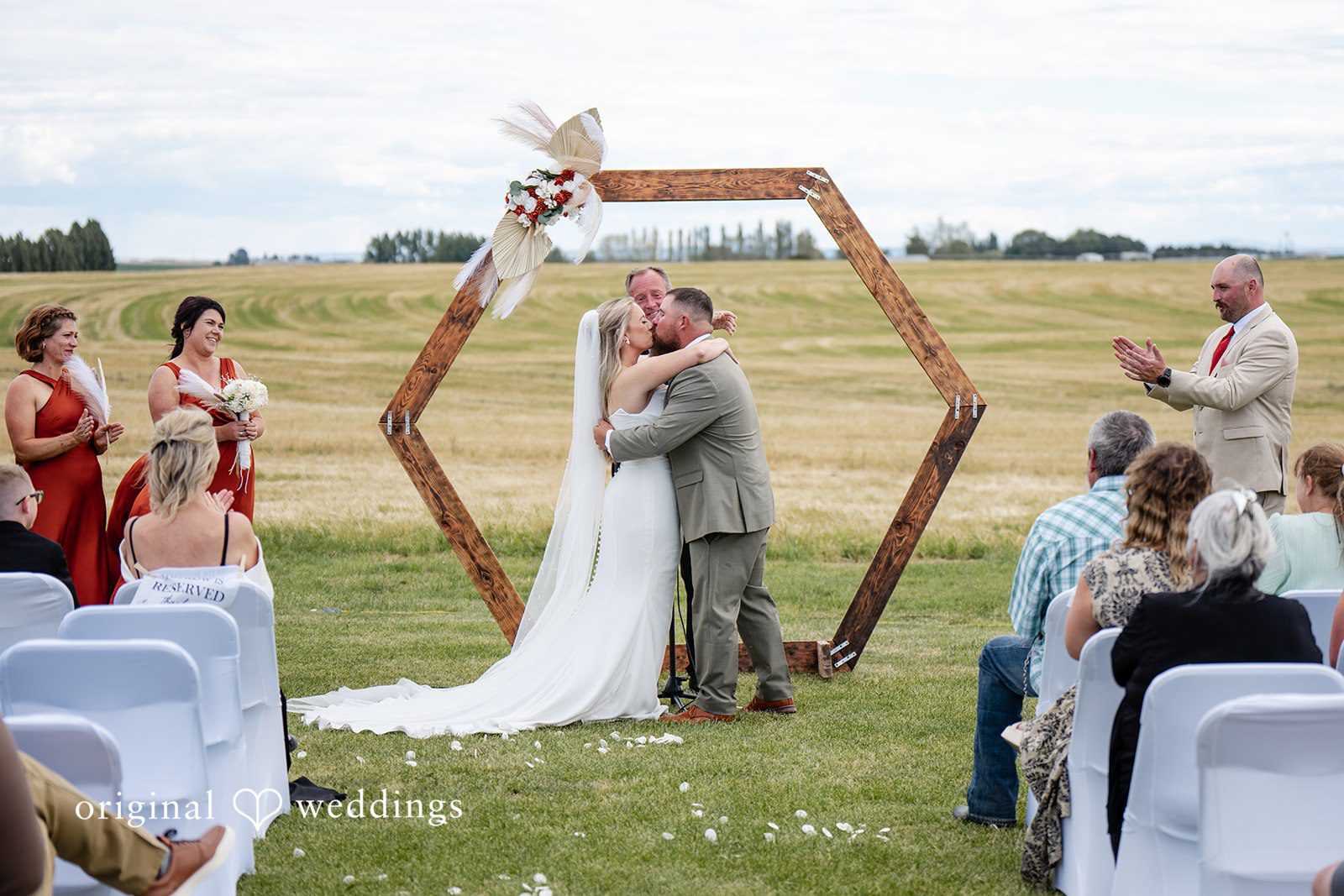Kayla + Dillon A newly married couple sharing a kiss beneath a hexagonal wooden wedding arch.