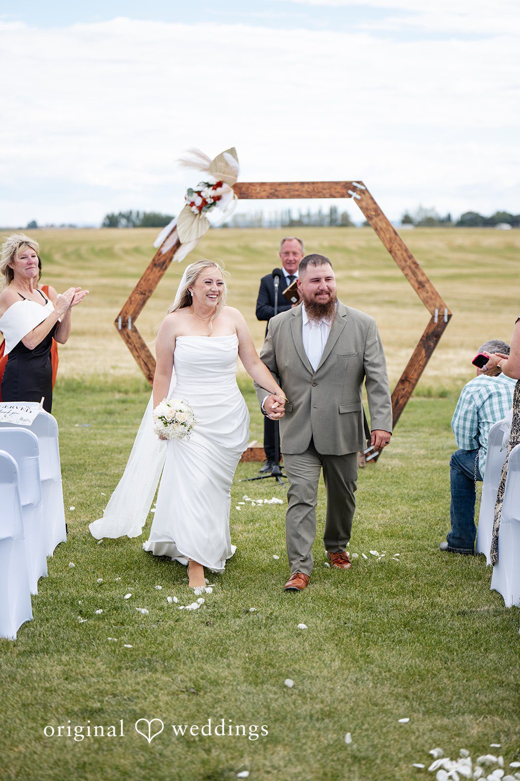 Kayla + Dillon A newly married bride and groom walking down the aisle together as guests cheer.