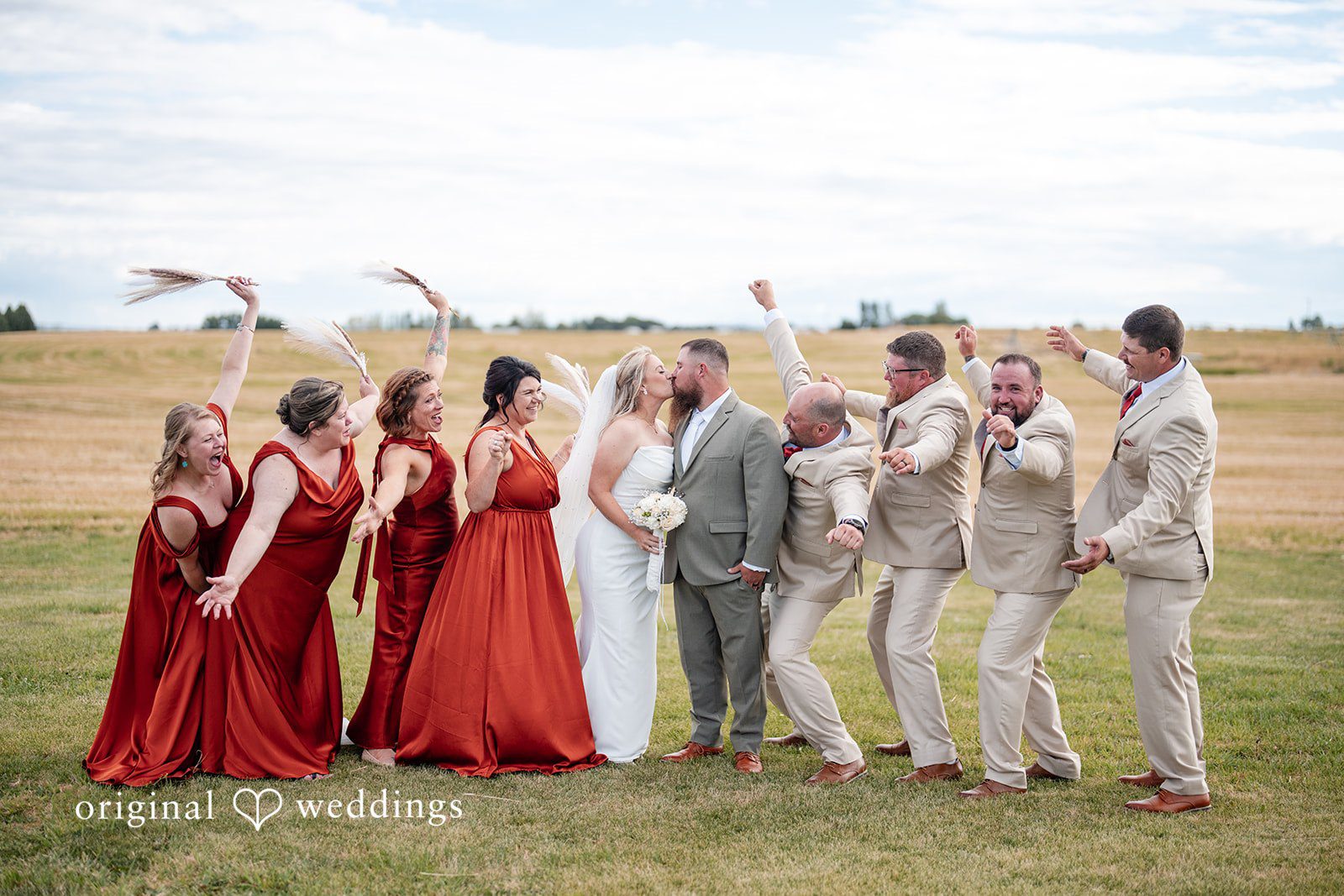 Kayla + Dillon A full wedding party posing in a line across a grassy field.