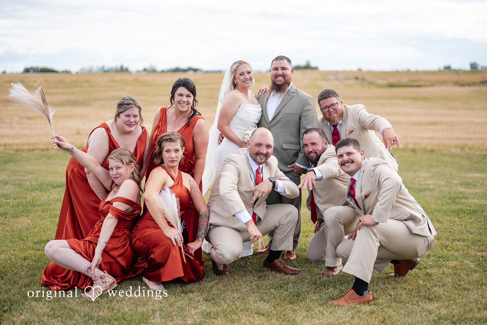 Kayla + Dillon A wedding party cheering and celebrating together in a wide open field.