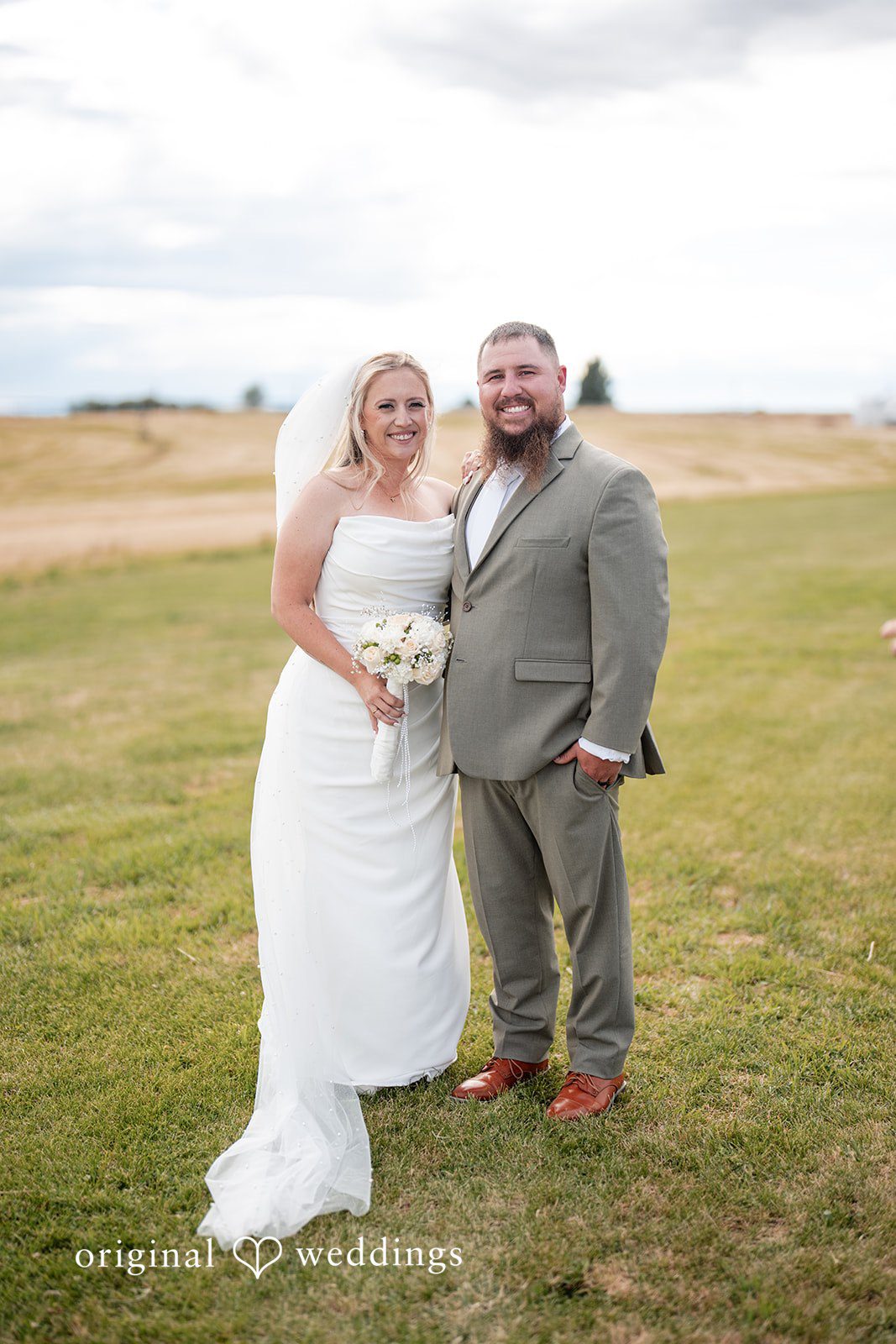 Kayla + Dillon A bride and groom smiling and posing together in a wide, open grassy field.