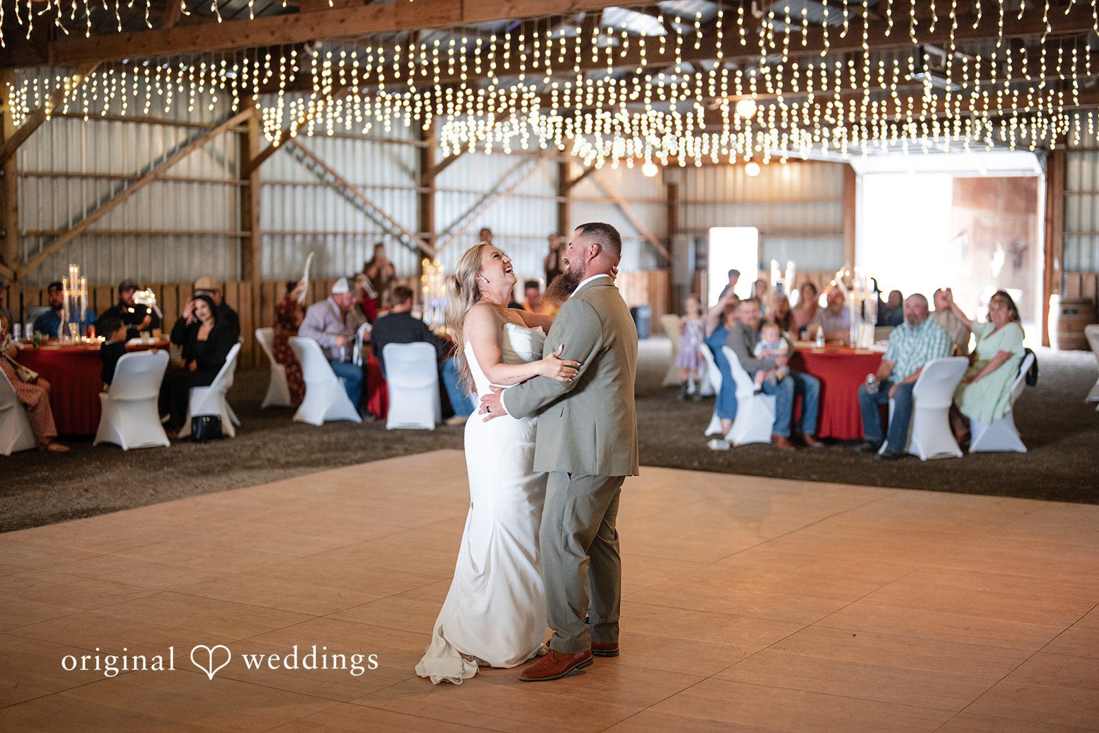 Kayla + Dillon A bride and groom sharing their first dance on a dance floor surrounded by wedding guests.