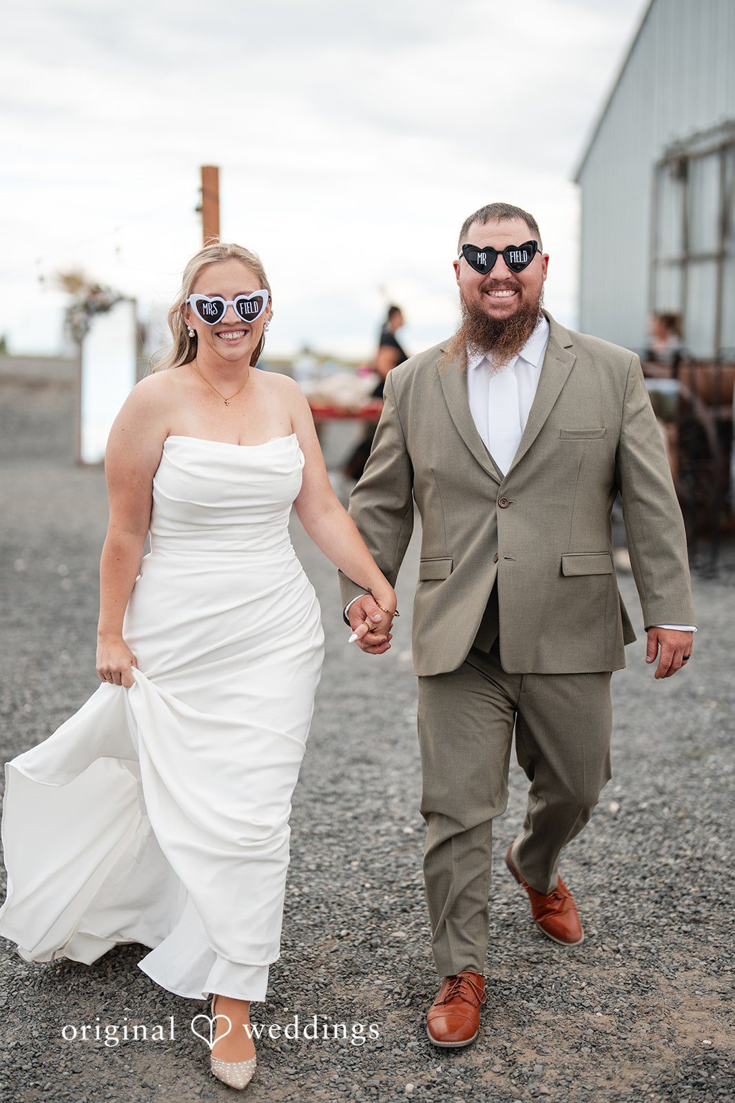 Kayla + Dillon A bride and groom wearing sunglasses while walking together on a gravel path.