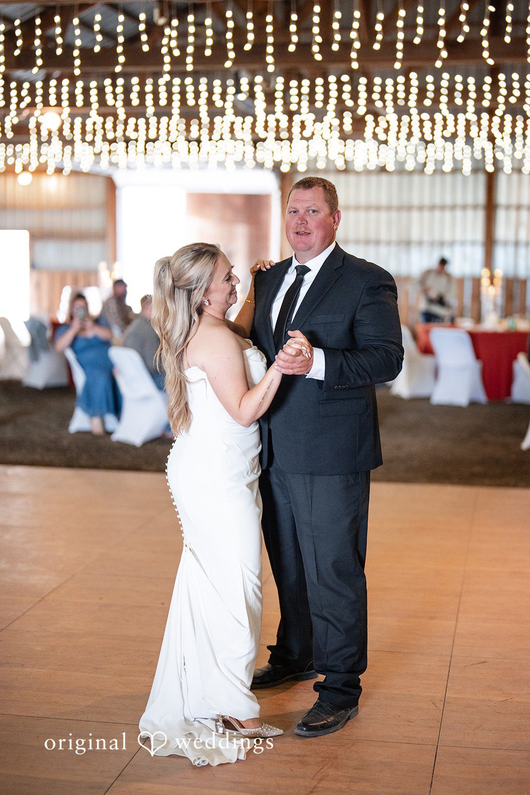 Kayla + Dillon A bride smiling while dancing with a male guest in a black vest at the reception.