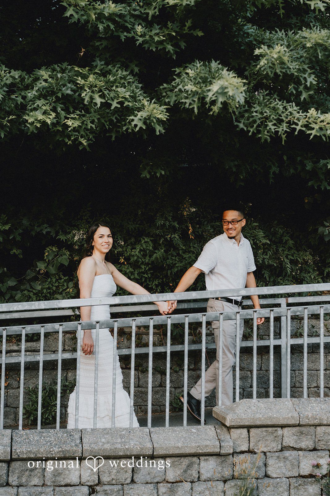 Couple holding hands while walking along a stone wall with metal railings.