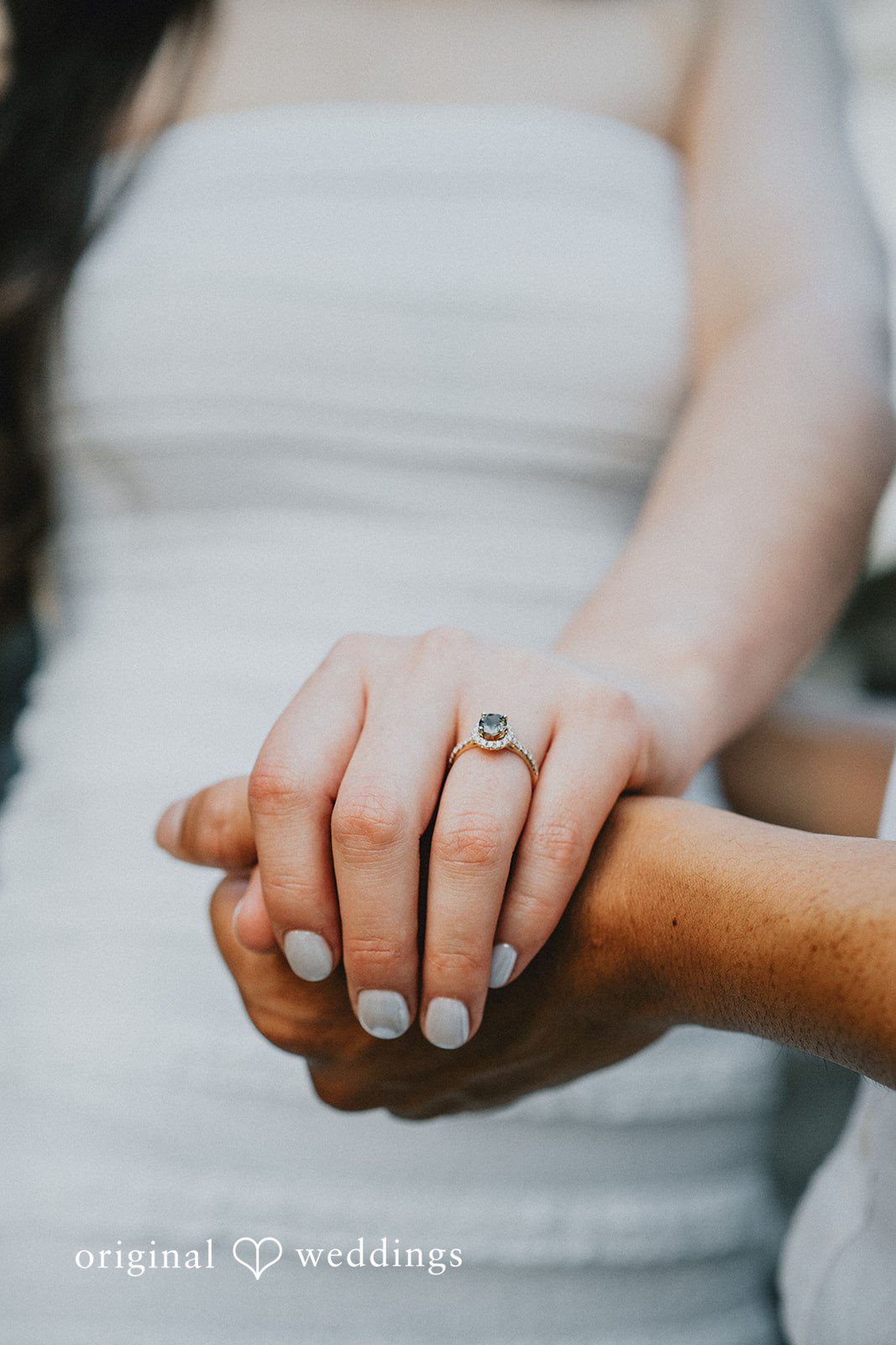 Close-up of a woman's hand wearing an engagement ring resting on a man's hand.