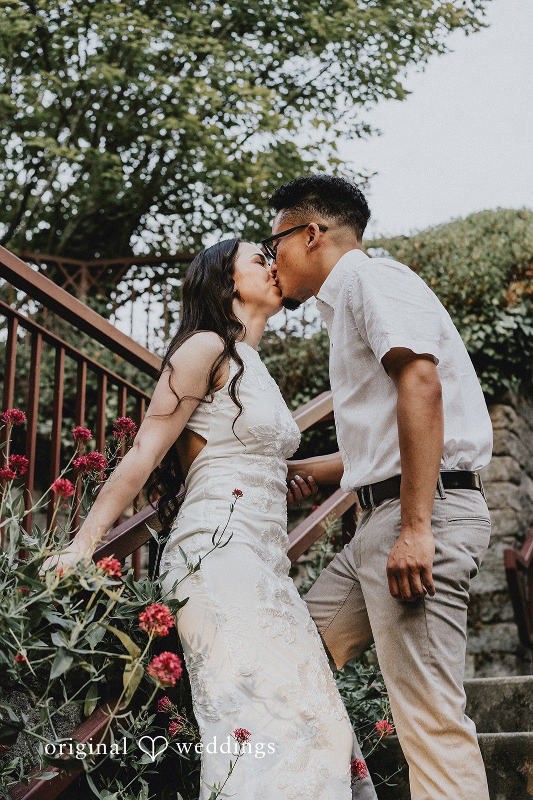 Couple sharing an intimate kiss next to a stone railing.
