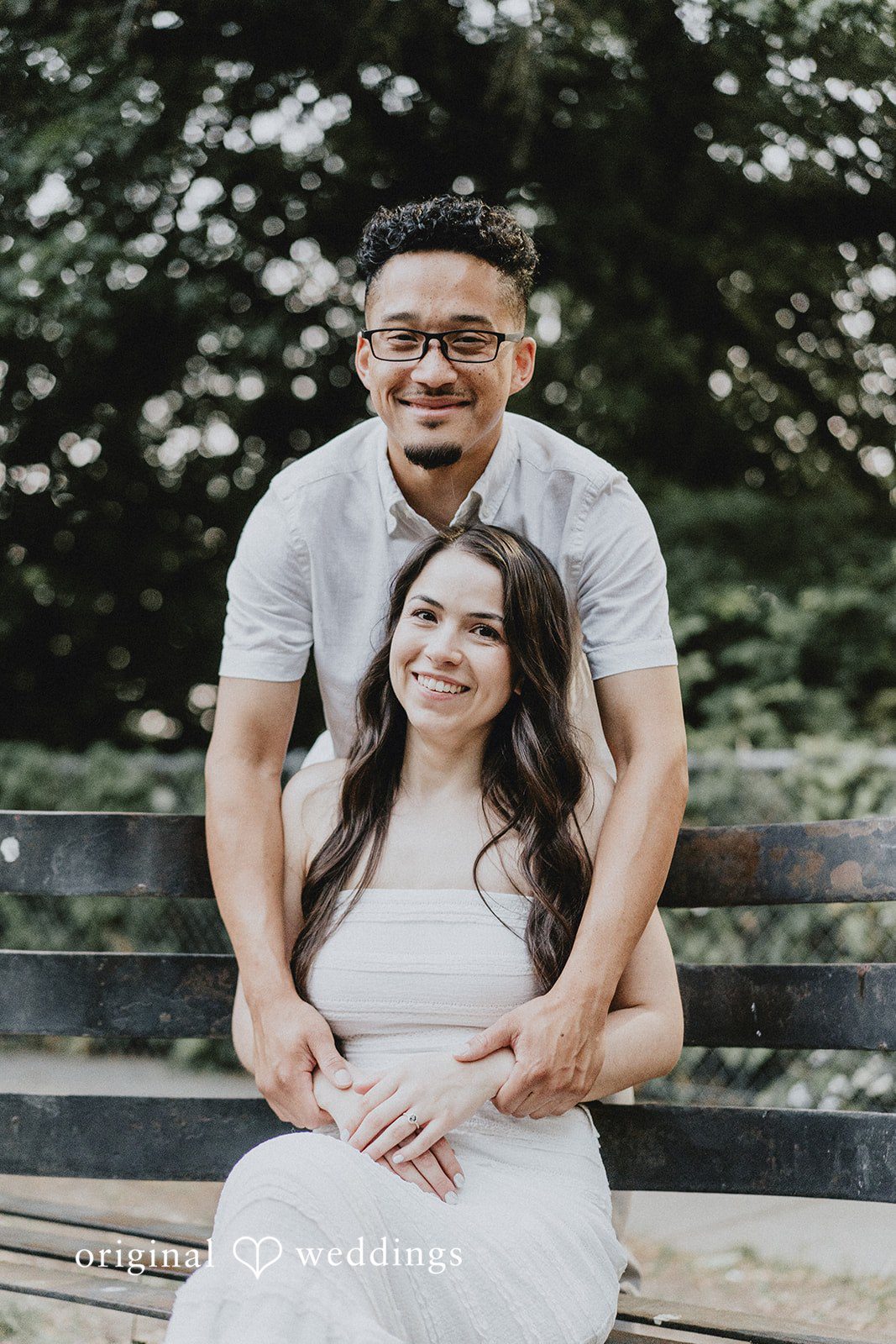 Man standing behind a smiling seated woman with his hands on her shoulders.