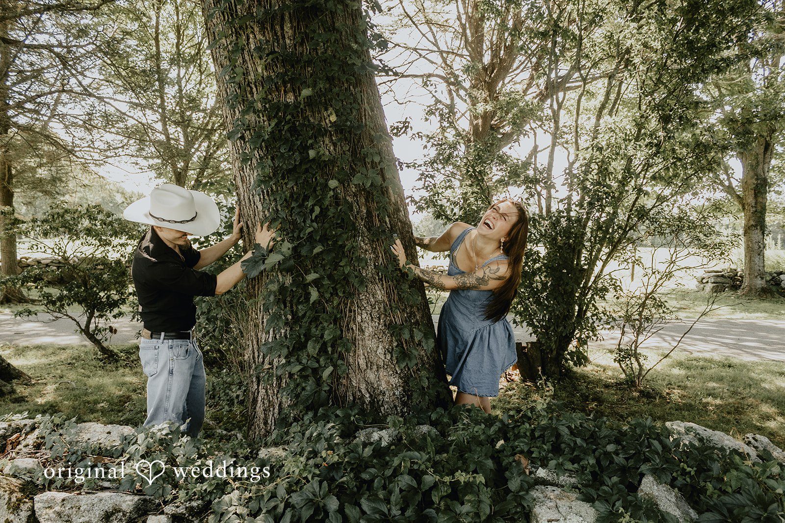 Meghan + Kal Couple stand near a large tree trunk in a wooded area.