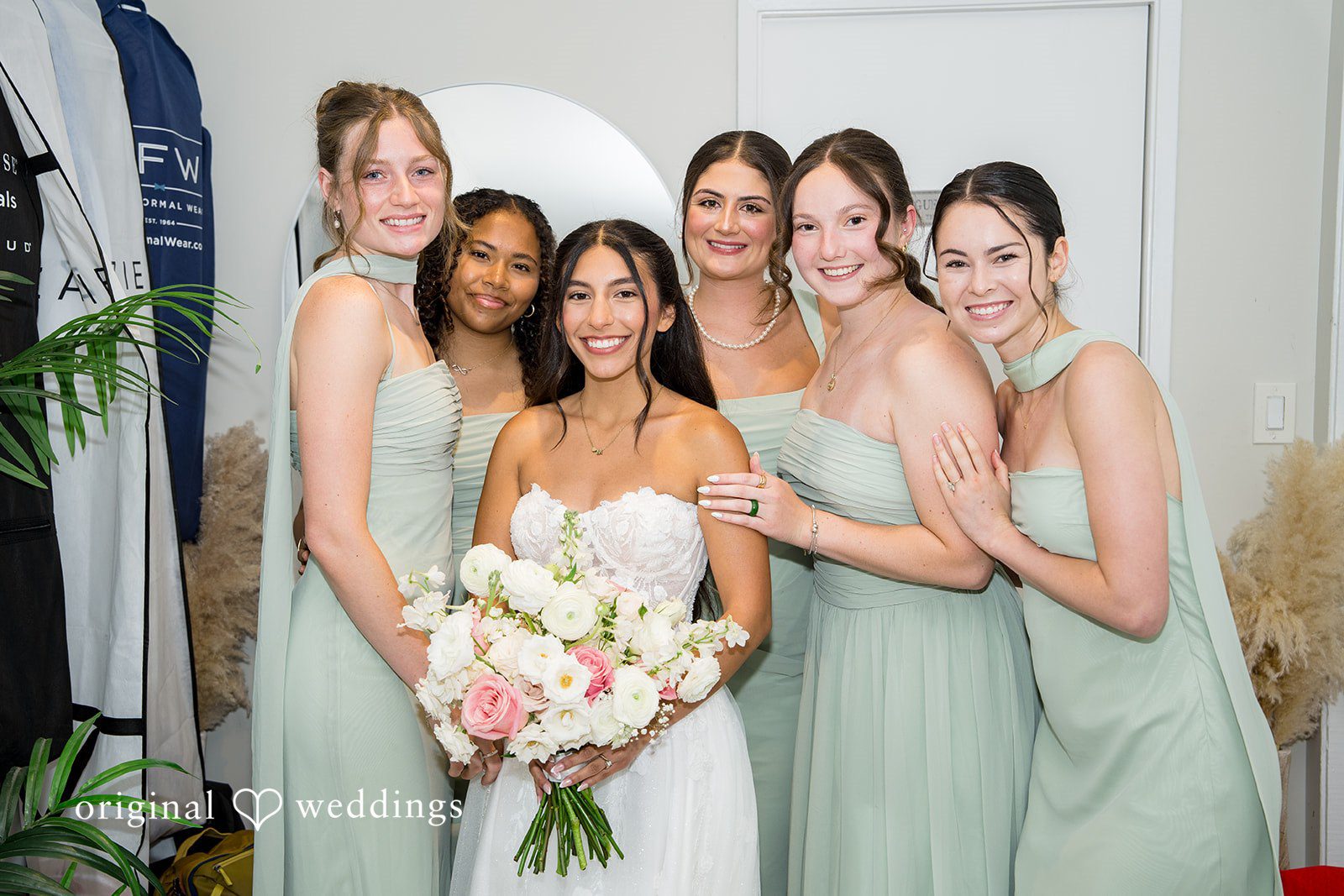 Kalina + Malakai A bride posing happily alongside four bridesmaids dressed in sage green gowns.