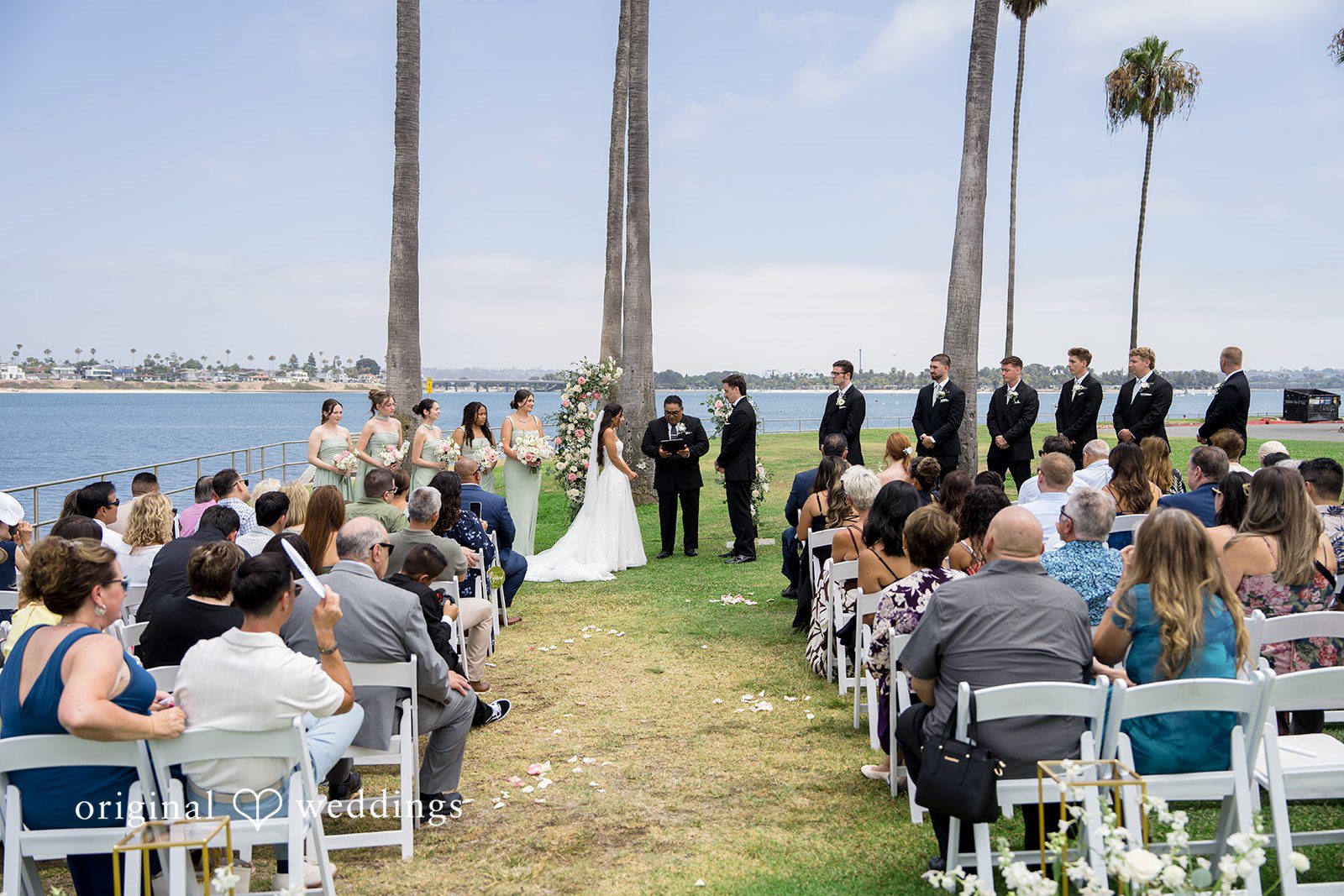 Kalina + Malakai An elevated view of guests seated for a wedding ceremony facing the waterfront.