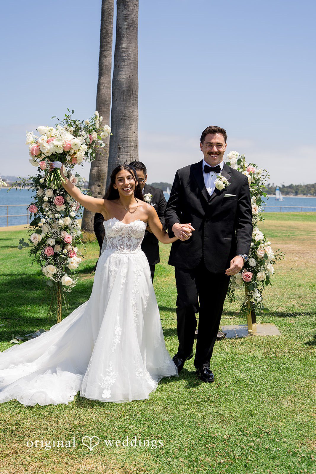 Kalina + Malakai Bride and groom walking down a concrete path lined with palm trees.