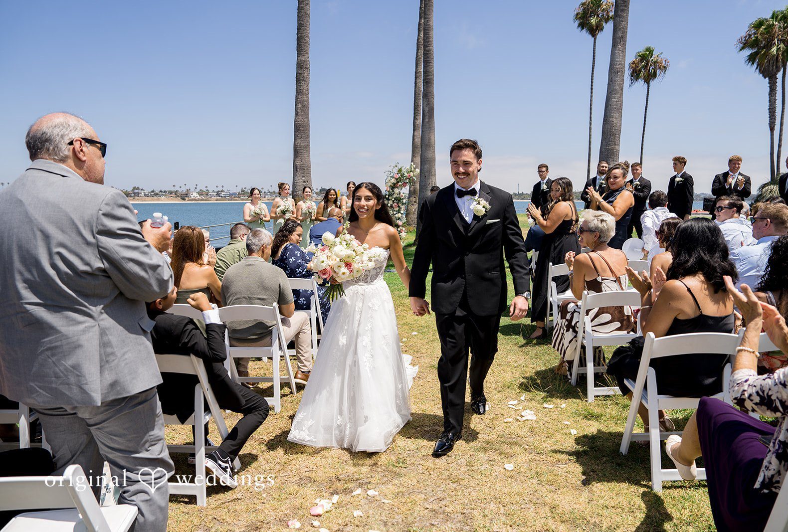 Bride and groom walking down the aisle while wedding guests applaud captured by San Diego Wedding Photographers from Original Weddings at Tower Beach Club