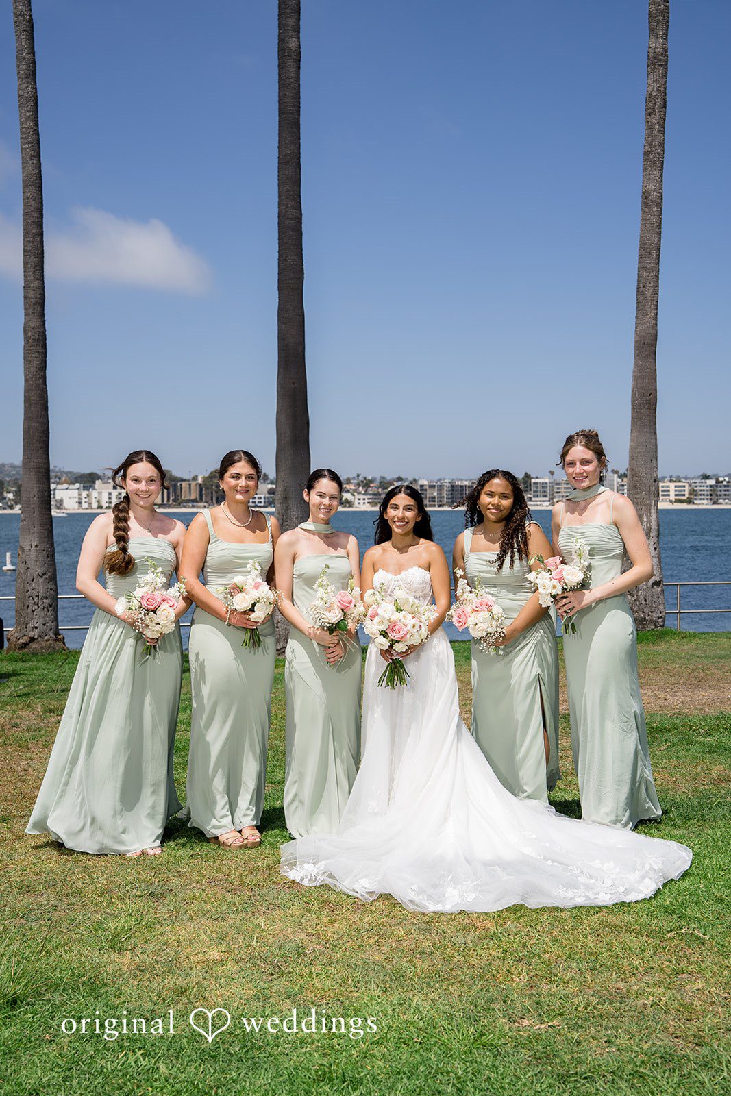 Kalina + Malakai The full wedding party posing together on a spacious green lawn.