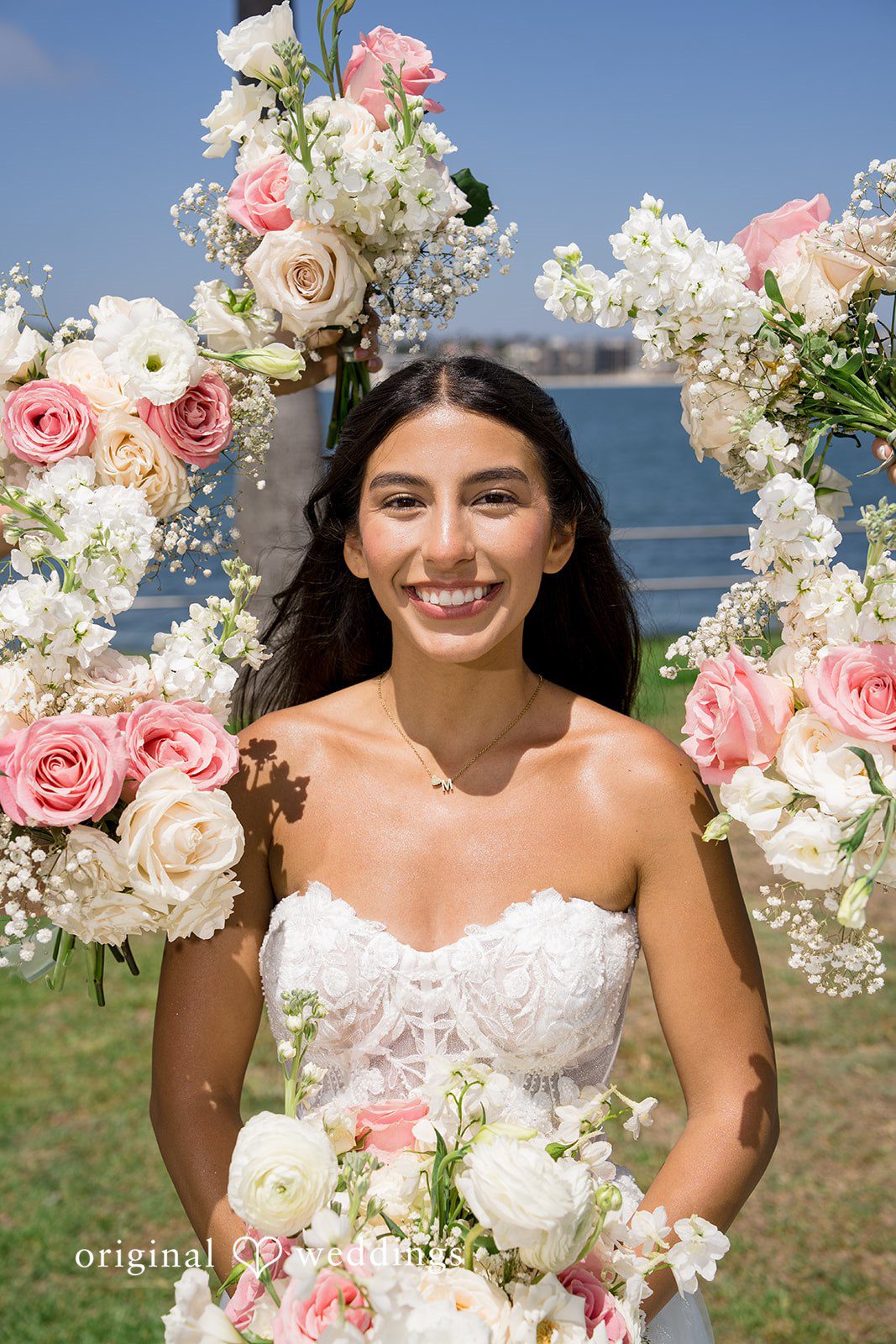 Kalina + Malakai A smiling bride holding a white bouquet in front of a colorful floral archway.