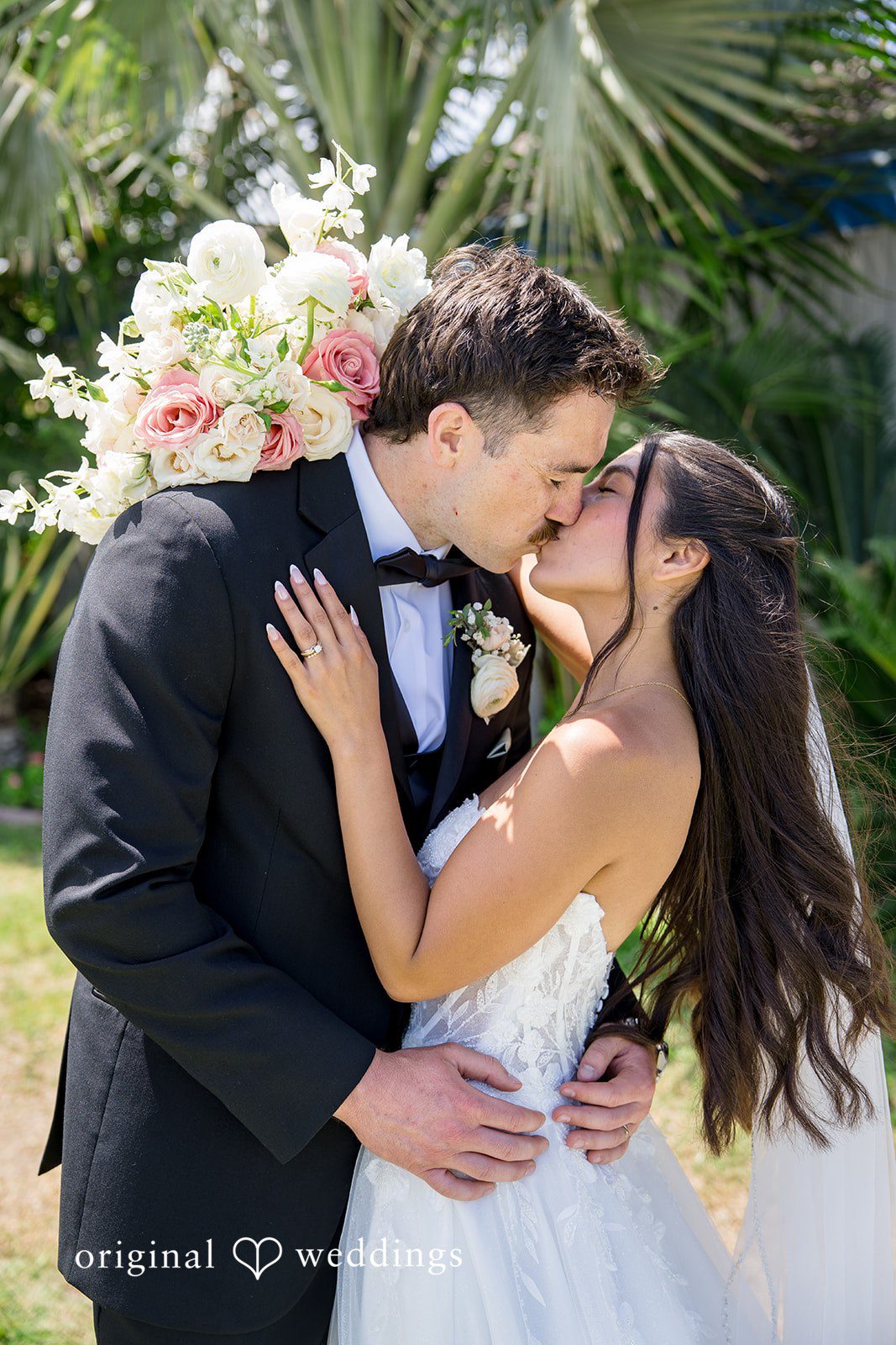 Kalina + Malakai Bride and groom kissing with lush green foliage in the background.