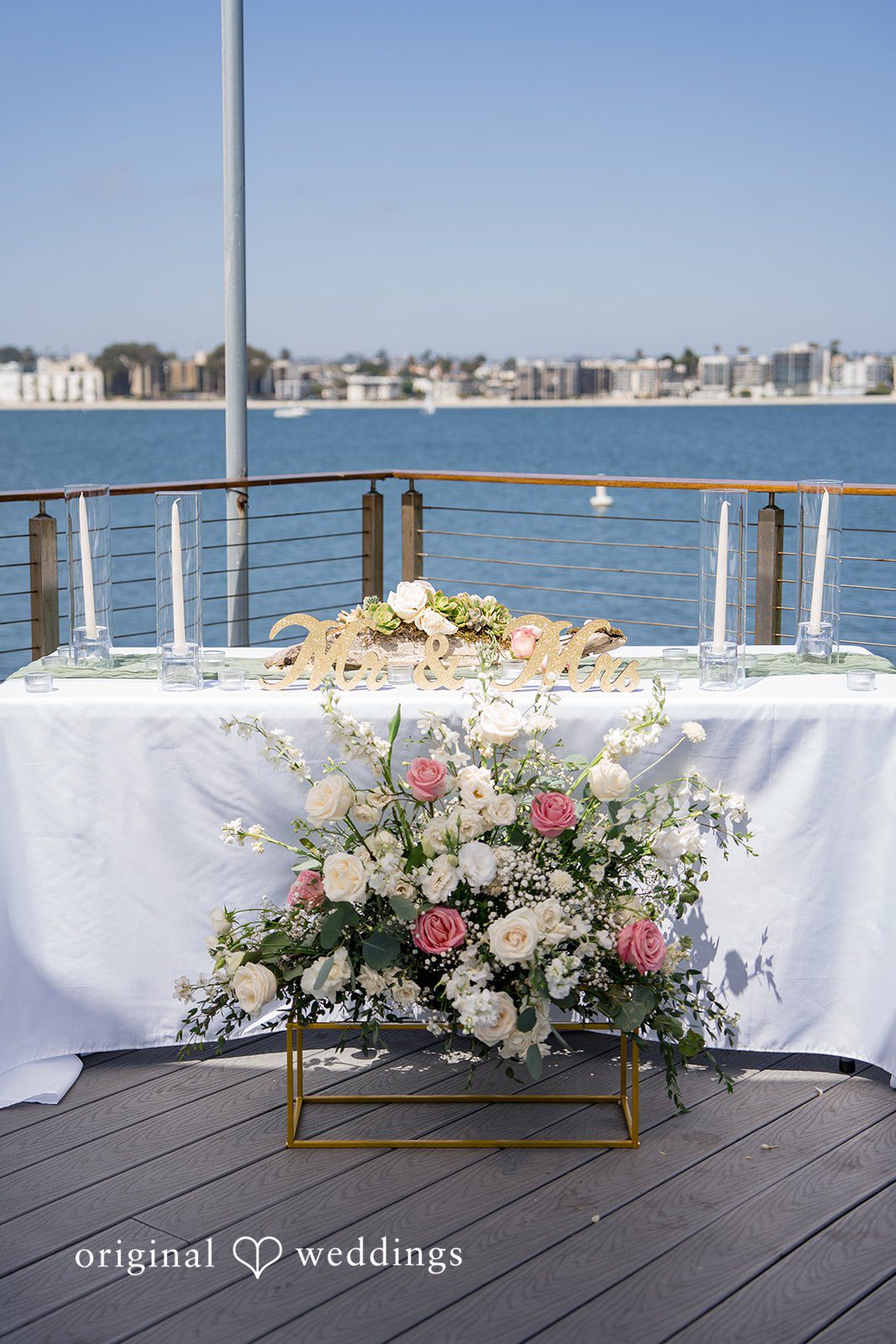 Kalina + Malakai A long banquet table draped in white cloth with pink and cream floral centerpieces.