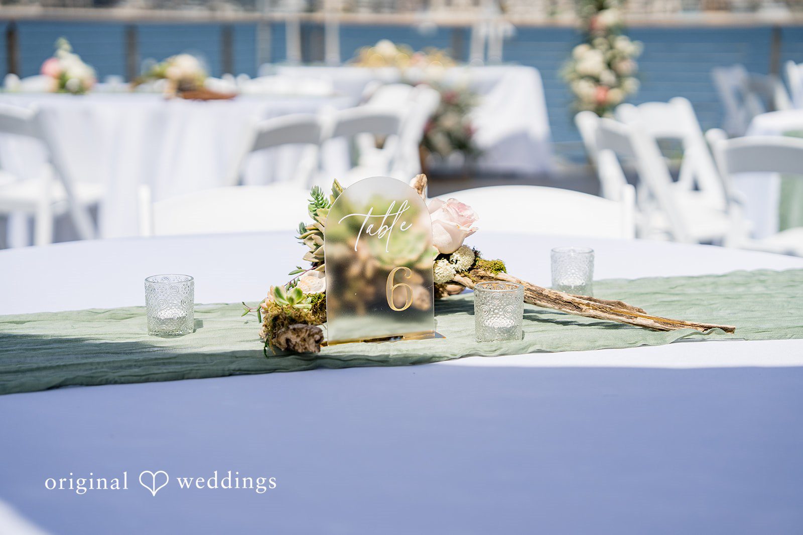 Kalina + Malakai A decorated wedding altar table with soft floral arrangements next to a waterfront.