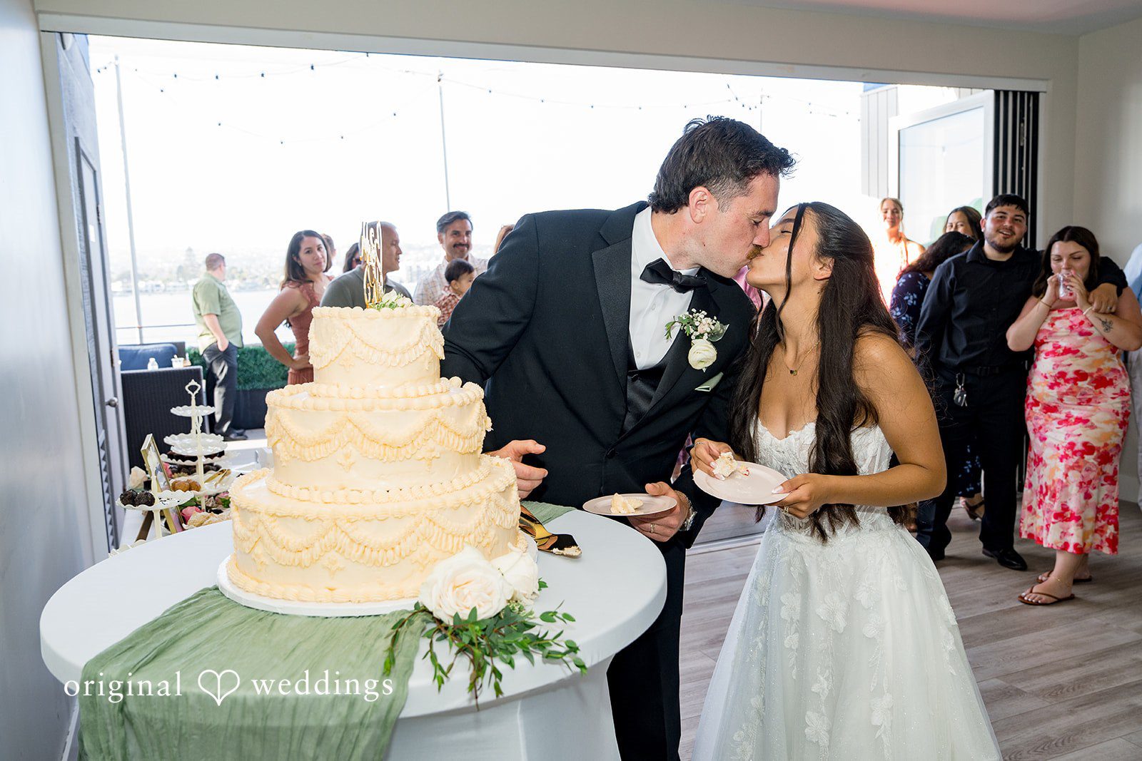 Kalina + Malakai Bride and groom kissing next to their tiered wedding cake.
