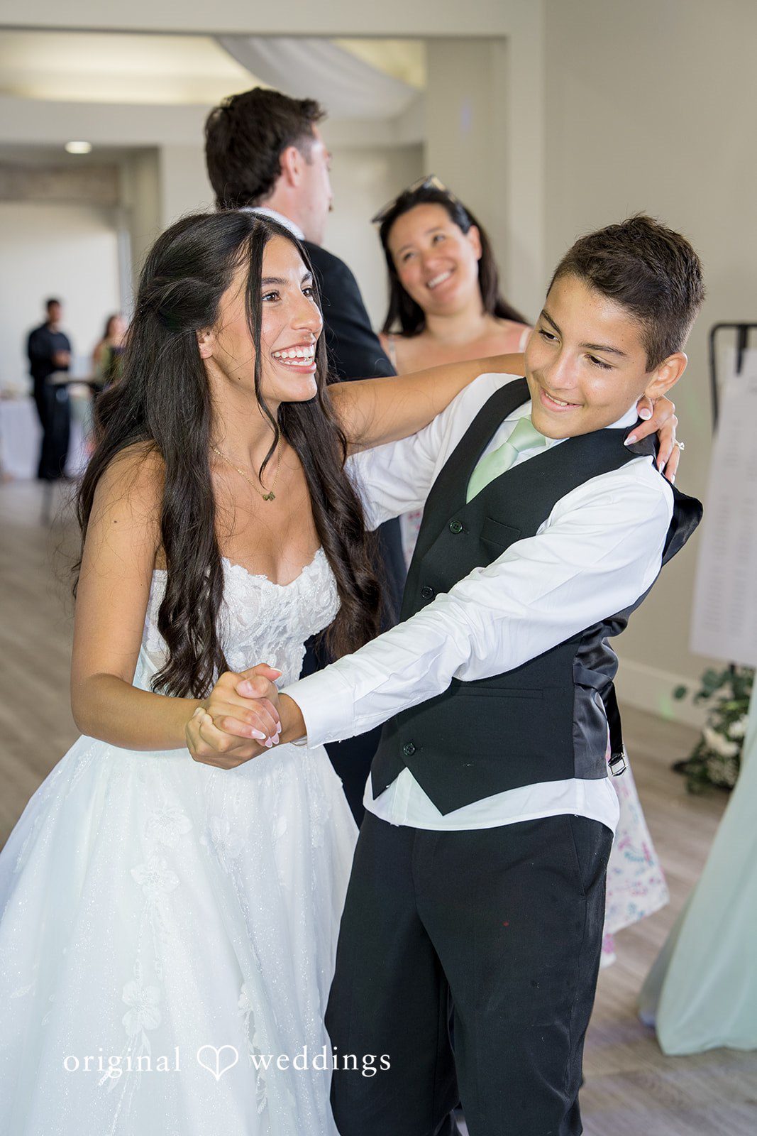 Kalina + Malakai A smiling bride sharing a playful dance with a young guest wearing a vest and tie.