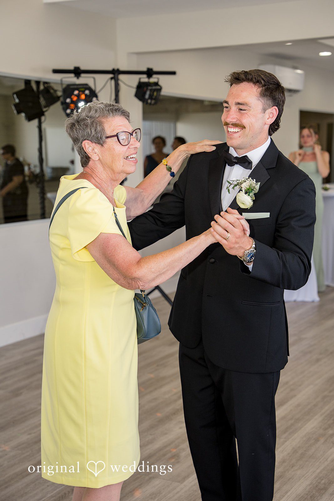Kalina + Malakai A groom in a black tuxedo dancing with a woman wearing a bright yellow dress.