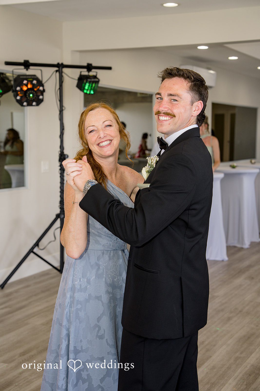 Kalina + Malakai A groom laughing while dancing closely with a guest in a light grey dress.