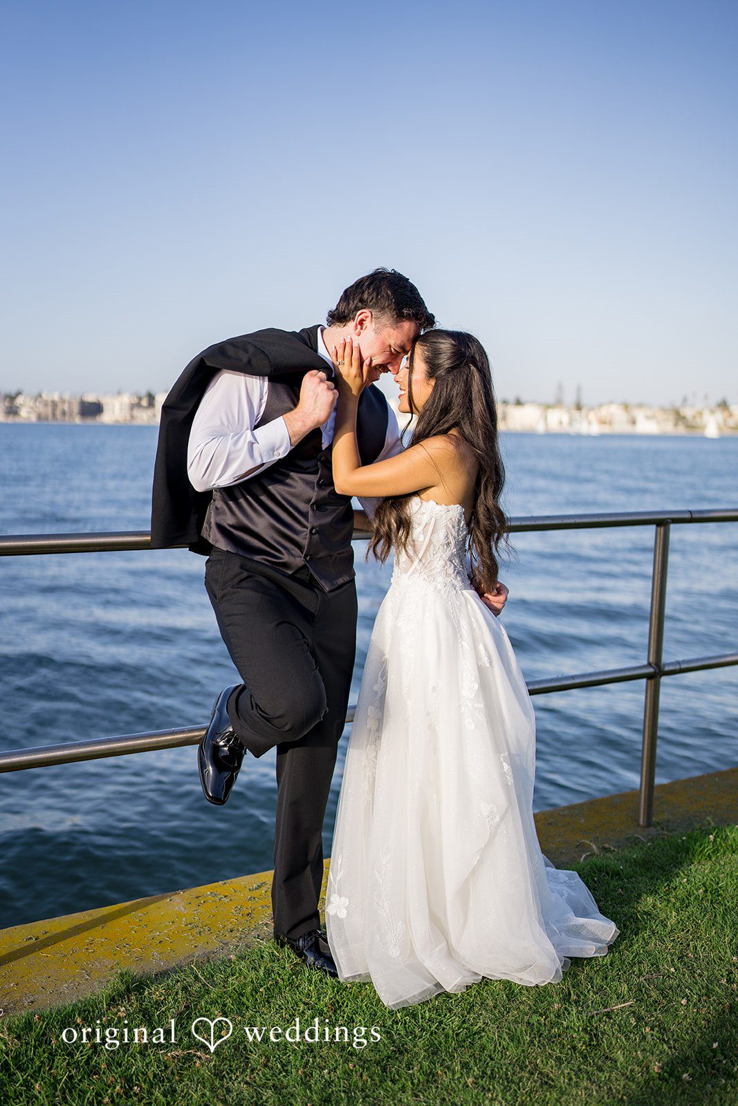 Kalina + Malakai Groom holding the bride close near a waterfront railing.