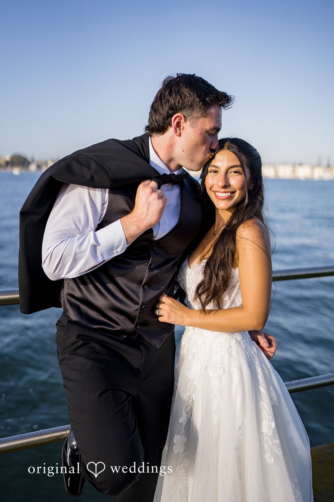Kalina + Malakai Bride and groom sharing a kiss on a walkway with sailboats behind them.