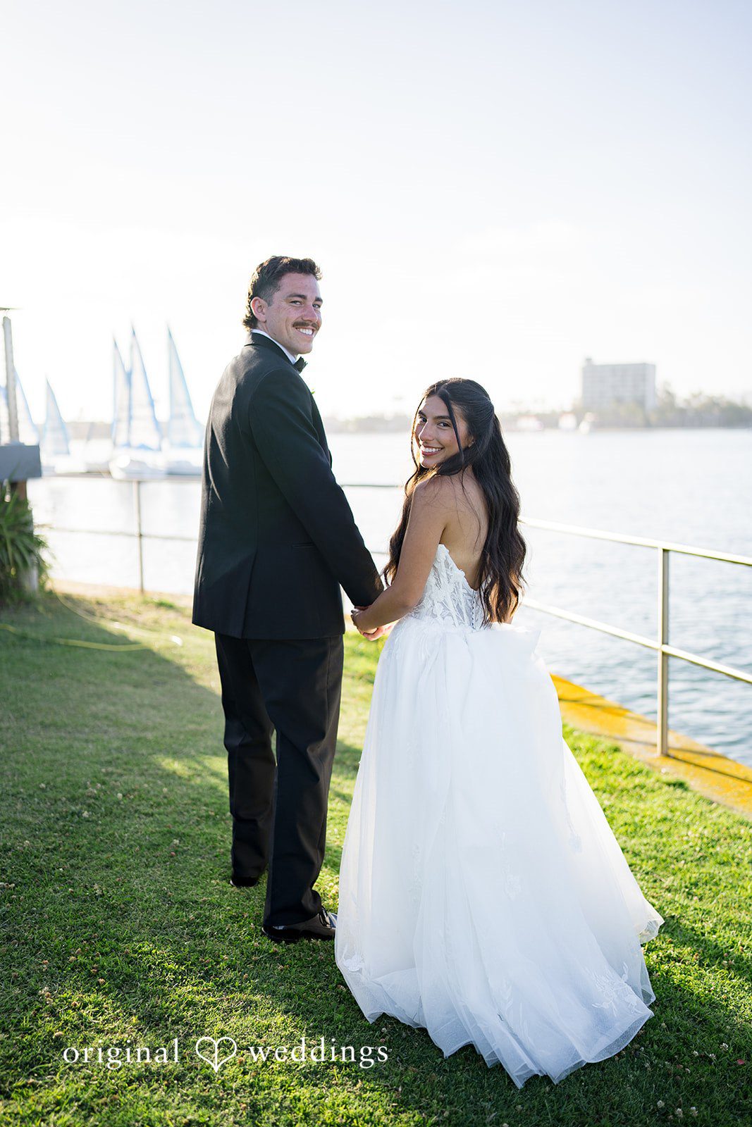 Kalina + Malakai Bride and groom holding hands while looking out at the water.