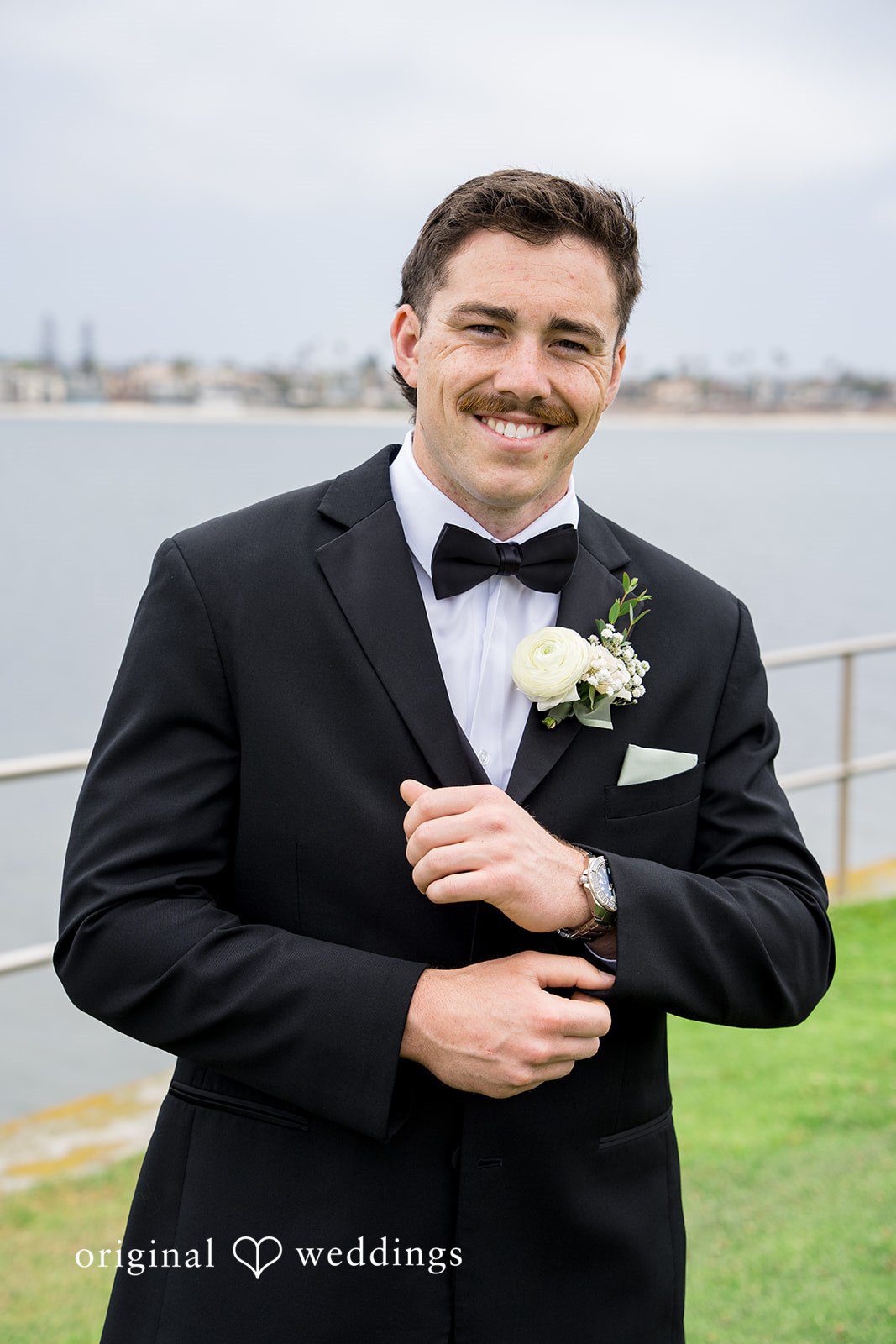 Kalina + Malakai A portrait of a groom smiling in a classic black tuxedo and bow tie.