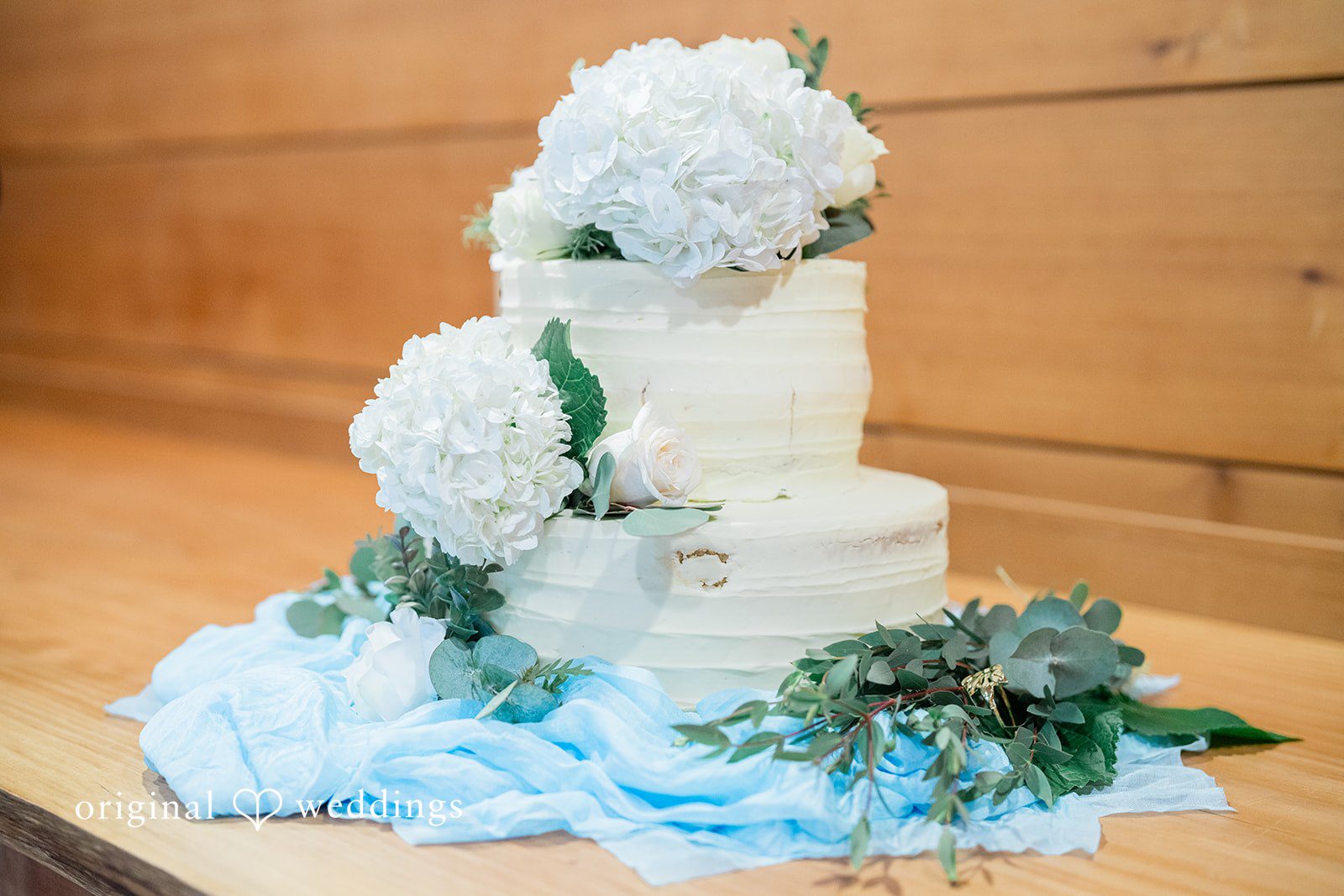 Destiny + Maksim A multi-tiered white wedding cake decorated with light blue flowers.