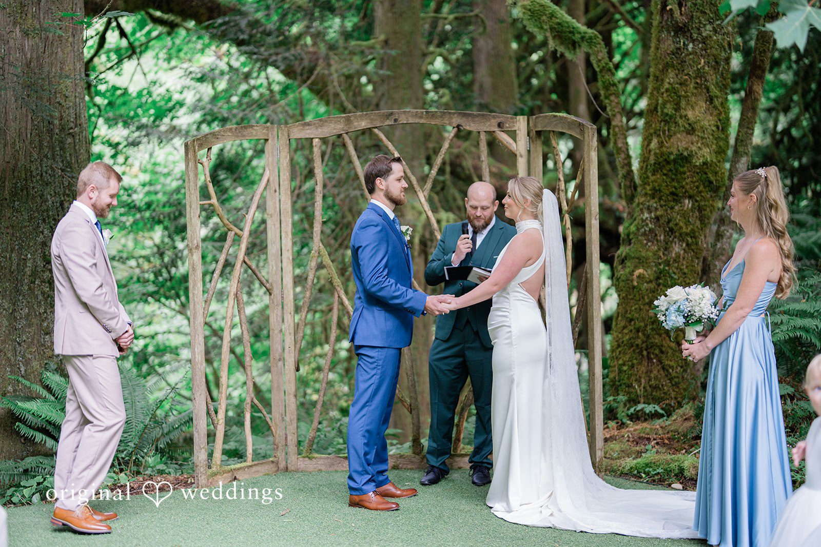 Destiny + Maksim A wedding ceremony taking place in front of a wooden arbor in a wooded area.