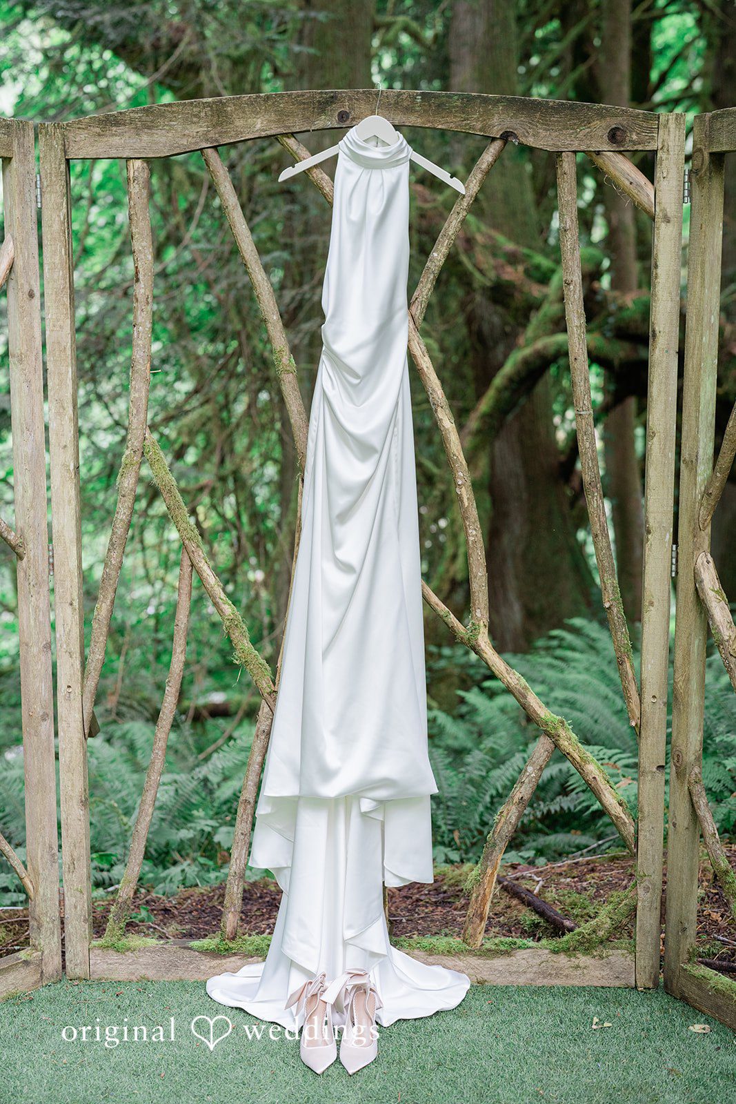 Destiny + Maksim A white wedding gown hanging on a wooden structure in a wooded area.