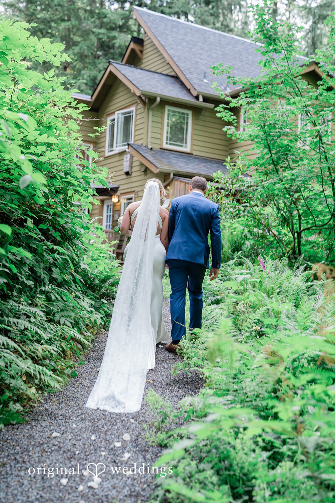 Destiny + Maksim A bride and groom walking away up a lush green path toward a house.