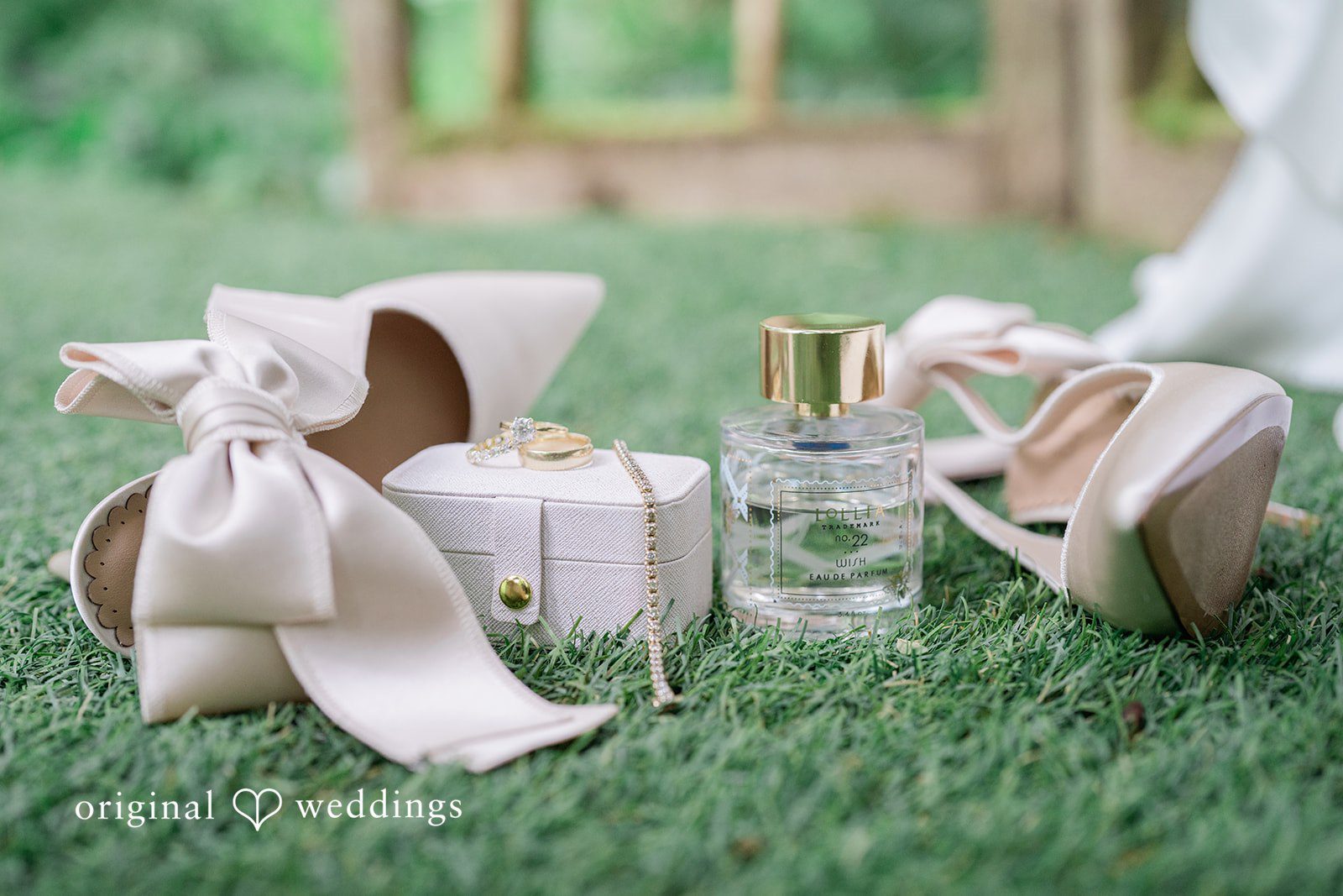 Destiny + Maksim A bridal flat lay with high-heeled shoes, perfume, and accessories on grass.
