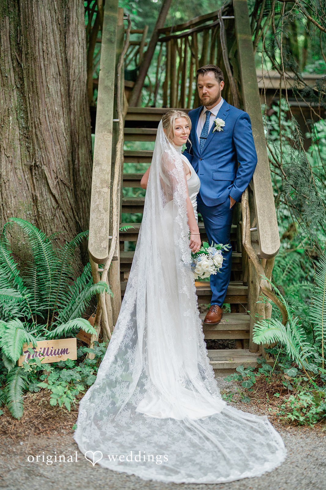 Destiny + Maksim A bride in her wedding gown posing on a wooden staircase in the woods.