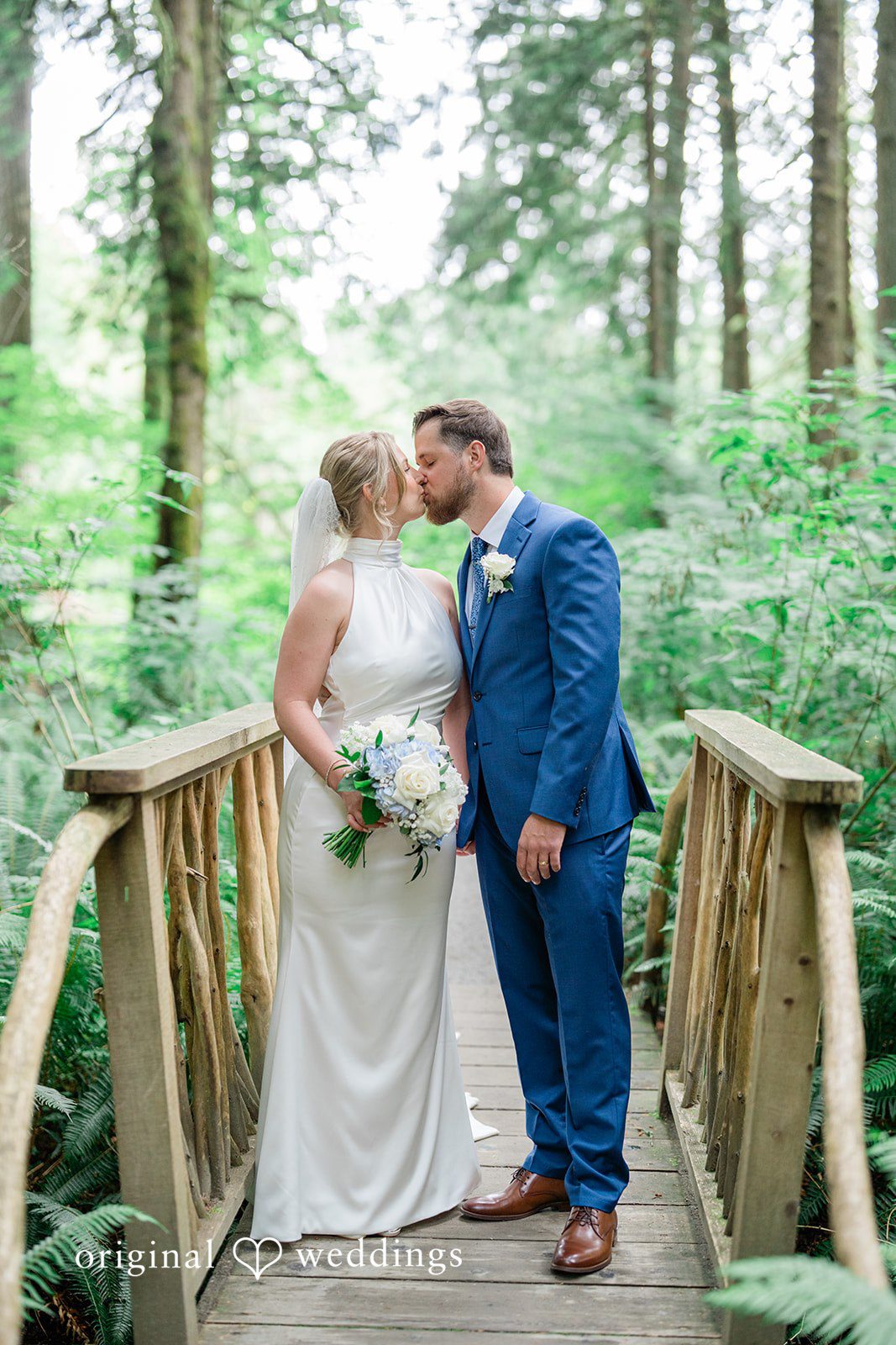 Destiny + Maksim A bride and groom sharing a kiss on a wooden footbridge in the woods.