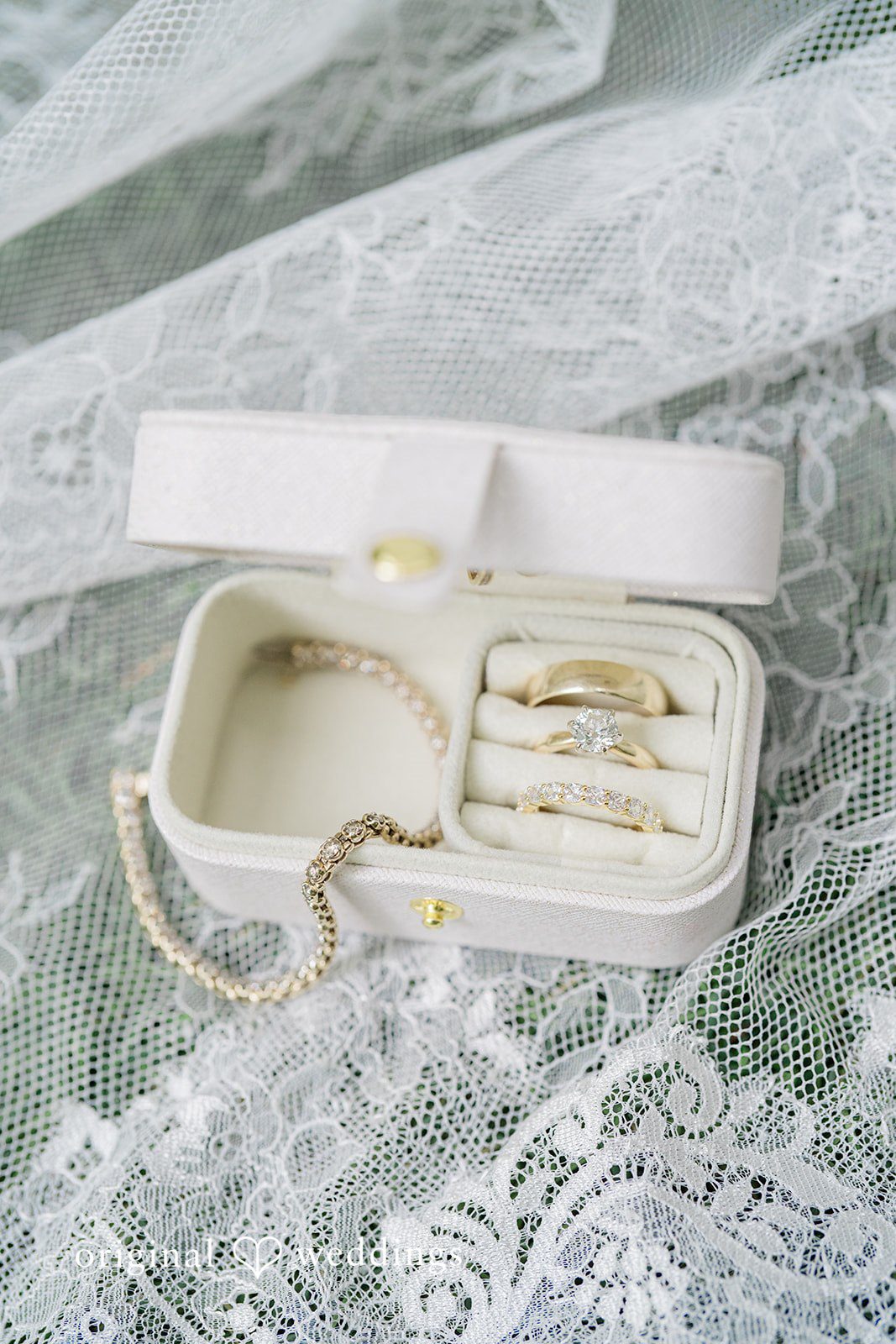 Destiny + Maksim An open white velvet jewelry box containing rings and earrings on lace fabric.
